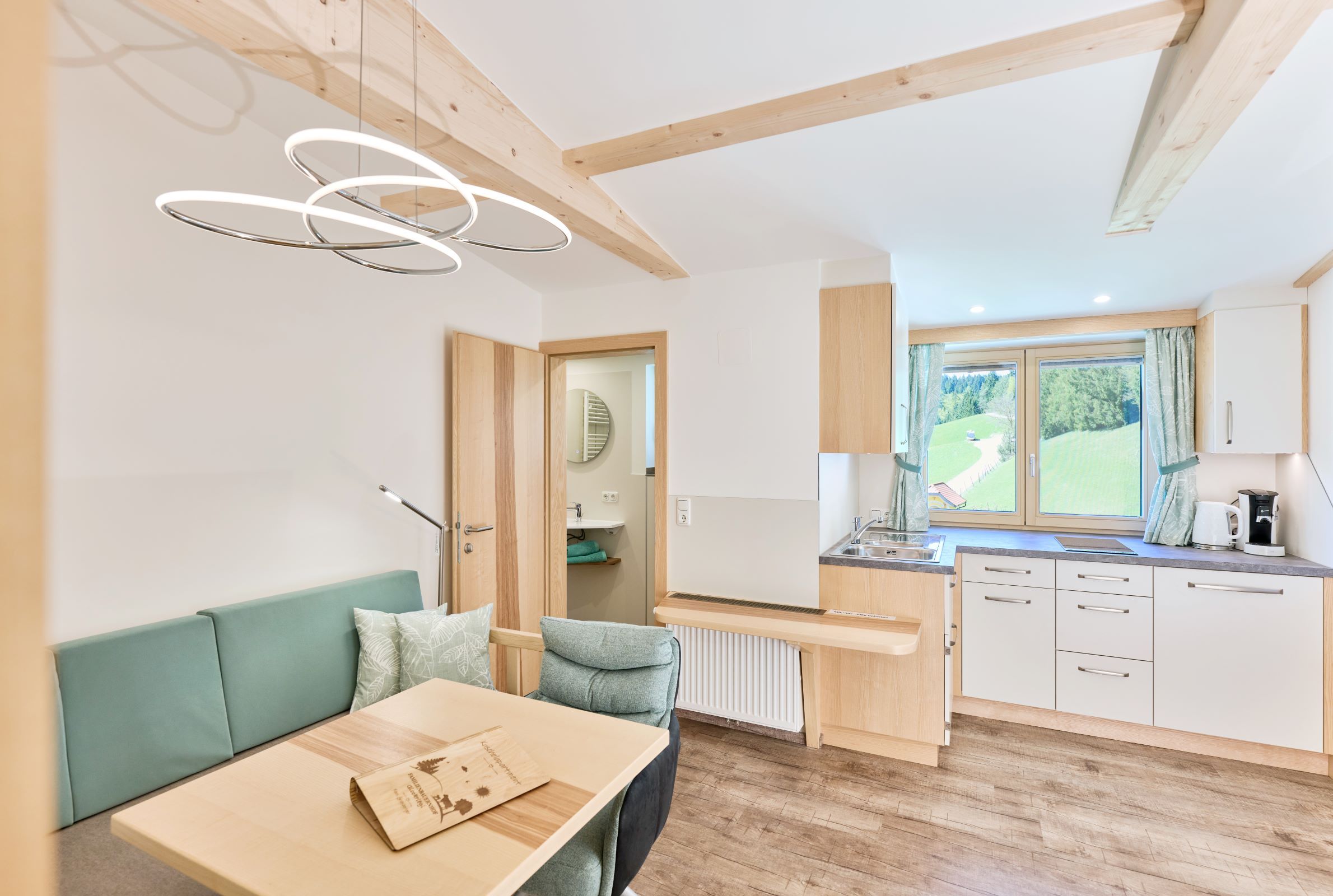 Modernes Apartment mit Holzelementen, Küchenzeile und Esstisch. Fenster mit Blick auf grüne Landschaft.