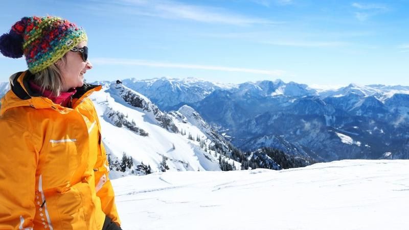 Frau in bunter Mütze und gelber Jacke blickt auf verschneite Berge.