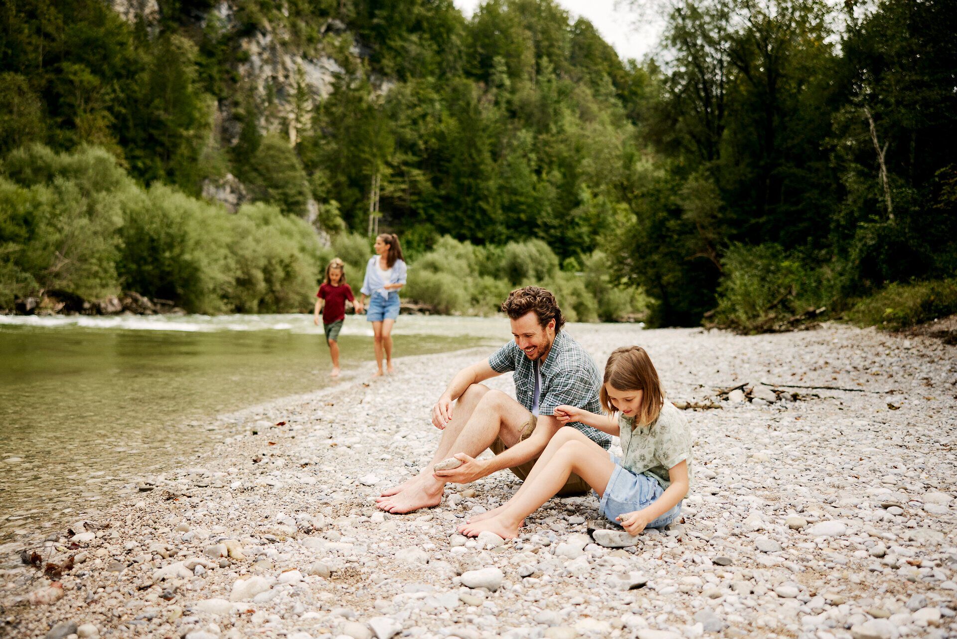An einem malerischen Flussufer genießen Familien die warmen Sonnenstrahlen und das erfrischende Wasser. Kinder lachen und spielen, während die Erwachsenen entspannen und die idyllische Natur rundherum bewundern. Diese harmonische Atmosphäre lädt dazu ein, die Schönheit des Sommers in vollen Zügen zu erleben.