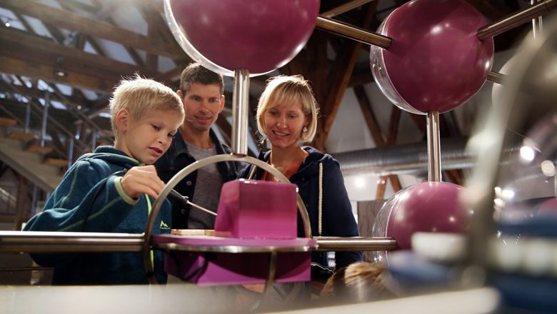 Eine Familie betrachtet eine interaktive Ausstellung mit großen, violetten Kugeln.