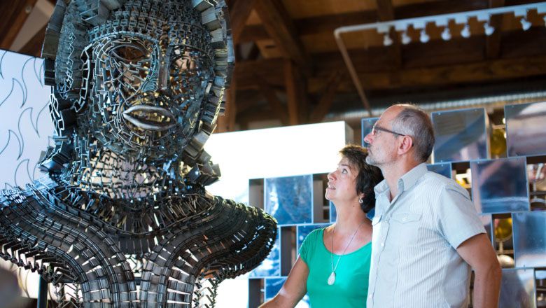Zwei Personen betrachten eine große Metallskulptur in einer Ausstellung.