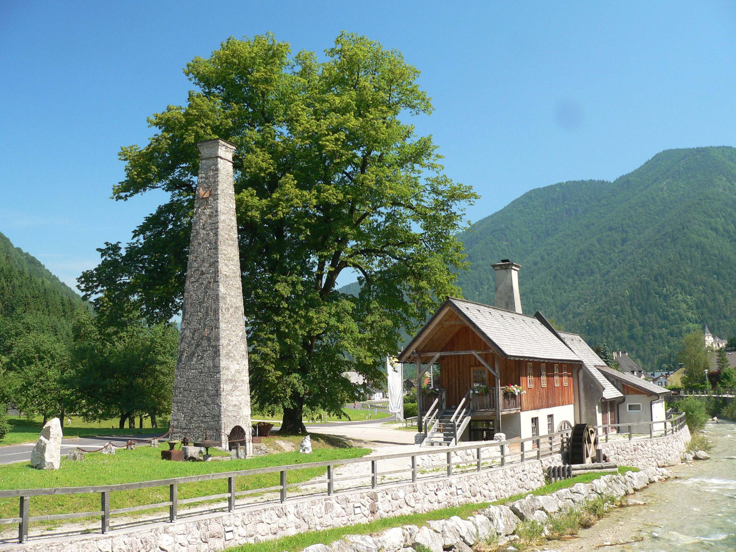 Historisches Gebäude mit Schornstein und Wasserrad in ländlicher Umgebung.