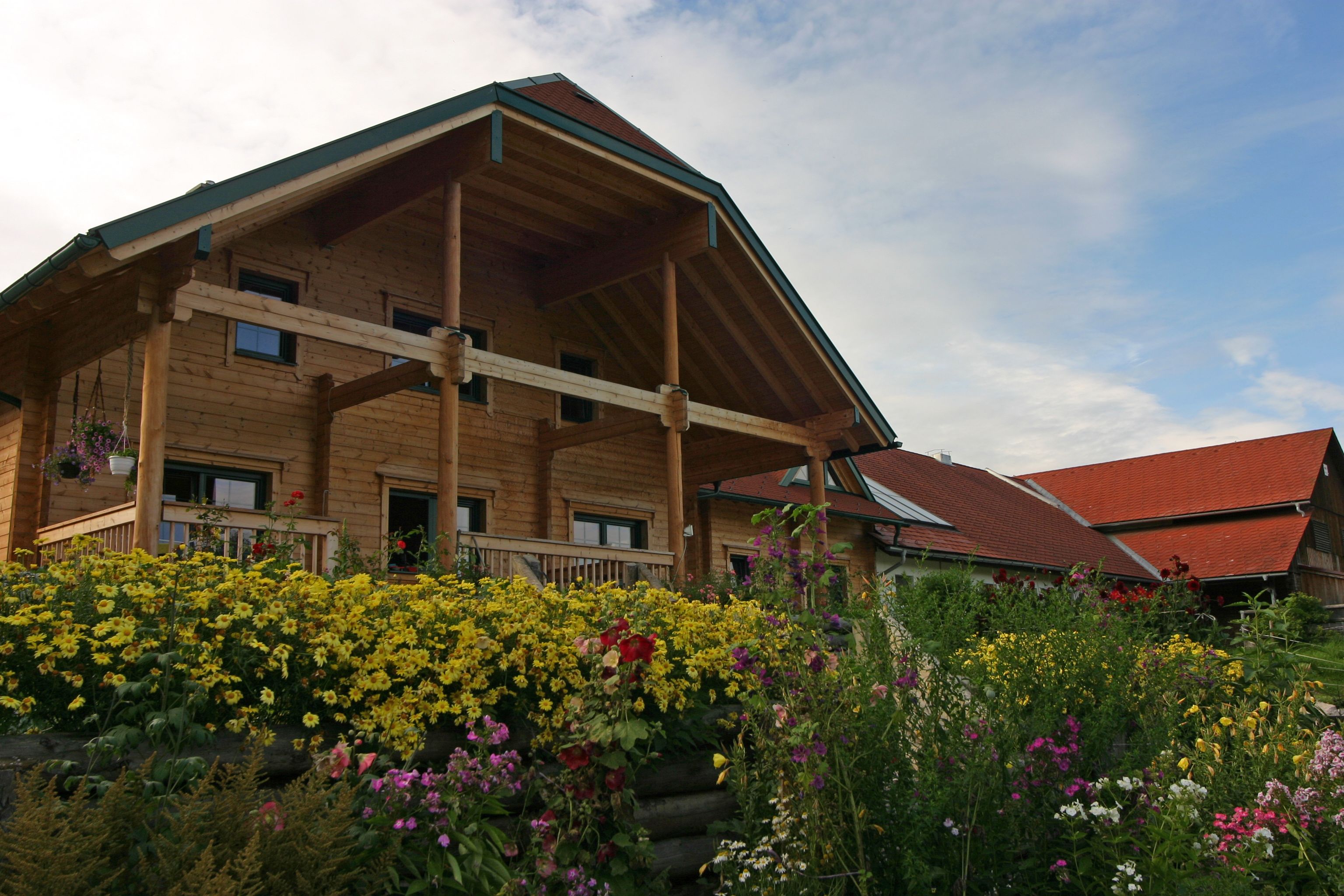Ein traditionelles Bauernhaus mit Holzverkleidung und einem blühenden Garten im Vordergrund.