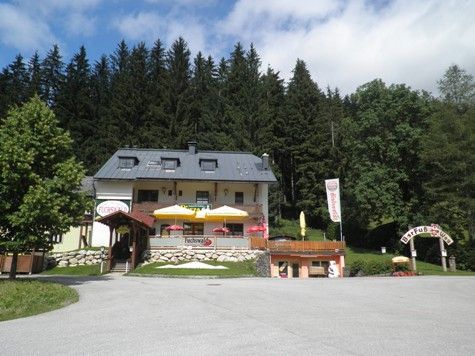 Ein Restaurant mit Terrasse und Sonnenschirmen vor einem Wald.