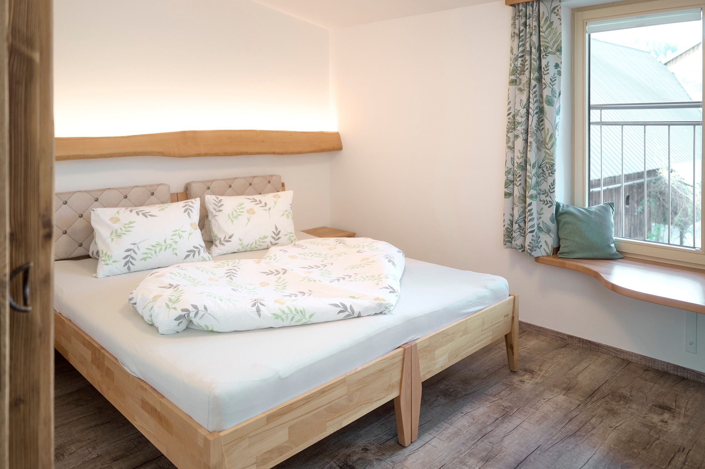 Gemütliches Schlafzimmer mit Doppelbett, Holzboden und Fenster mit Vorhängen.