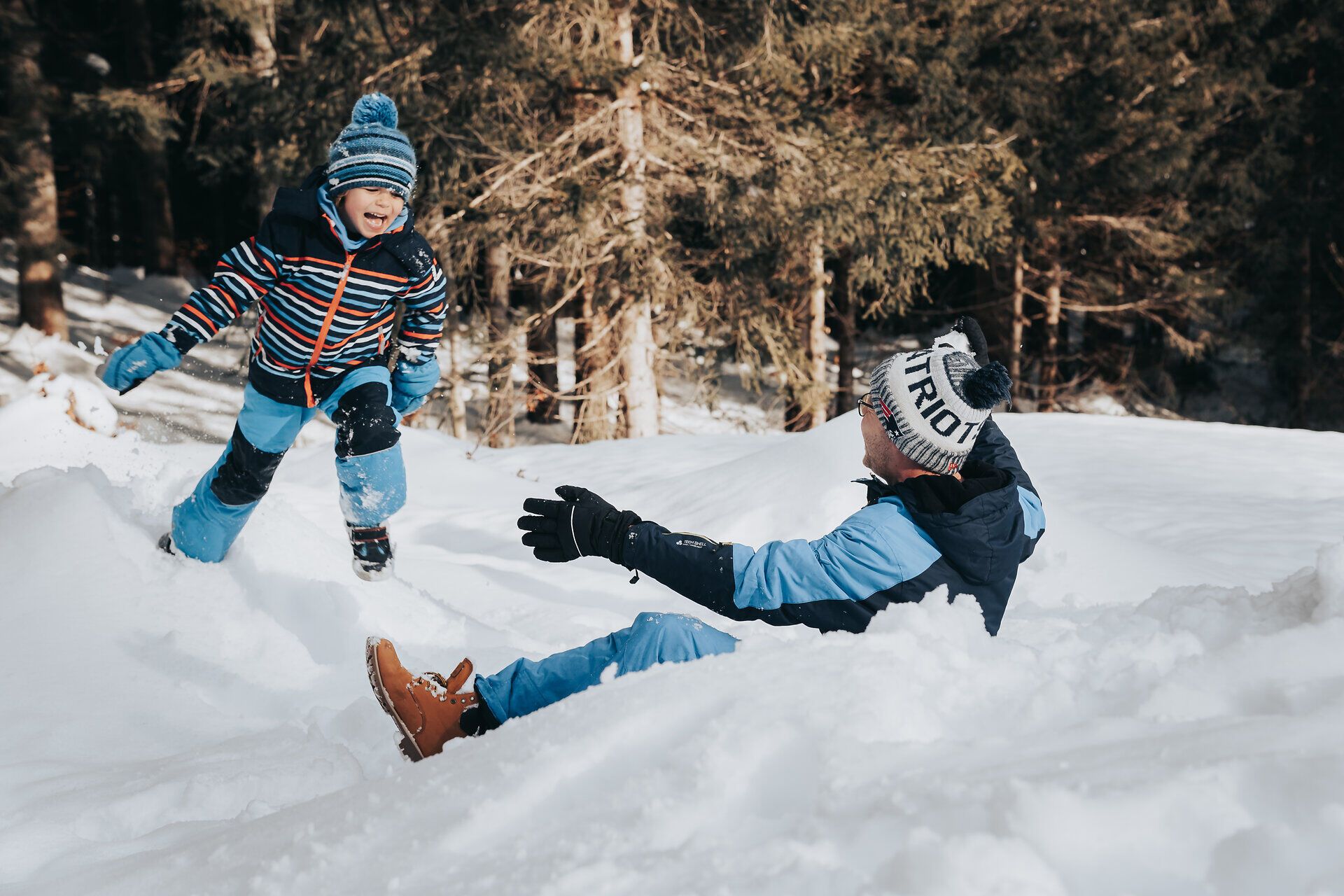 In der winterlichen Landschaft toben ein fröhlicher Junge und sein Vater im frischen Schnee. Die strahlende Sonne und die schneebedeckten Bäume schaffen eine zauberhafte Atmosphäre, die zum Spielen und Entdecken einlädt. Hier wird der Winter in den Ybbstaler Alpen zum unvergesslichen Erlebnis für die ganze Familie.