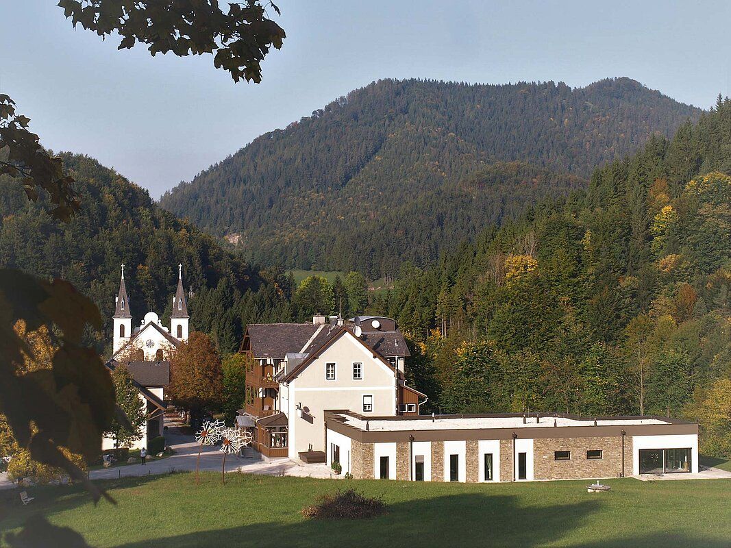 Gebäude des Fastenhauses Maria Seesal vor bewaldeten Hügeln.