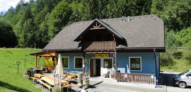 Ein blaues Gebäude mit Holzbalkon und Terrasse, umgeben von Bäumen.