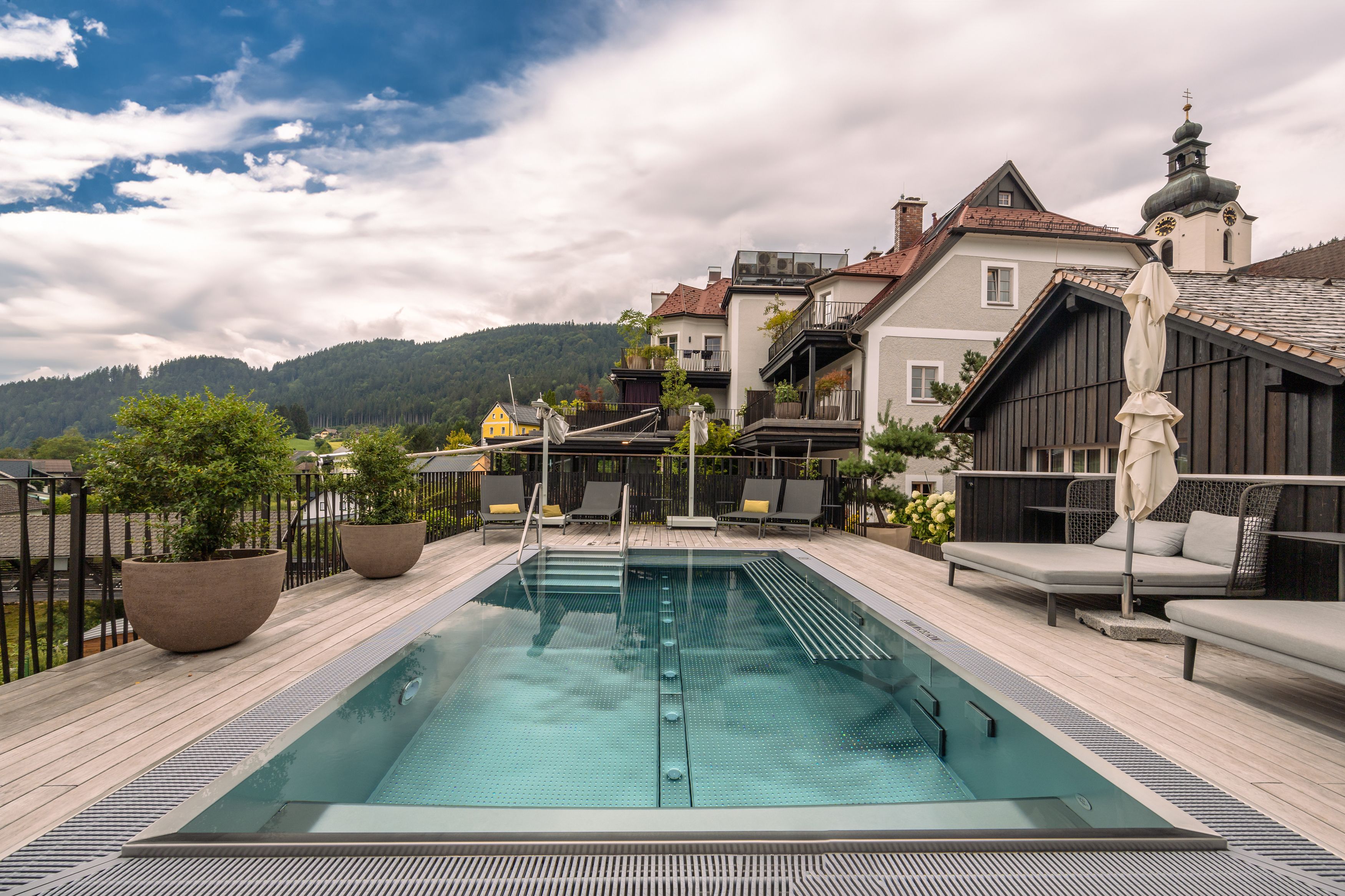 Ein moderner Pool auf einer Terrasse mit Blick auf umliegende Häuser und bewaldete Hügel im Hintergrund.