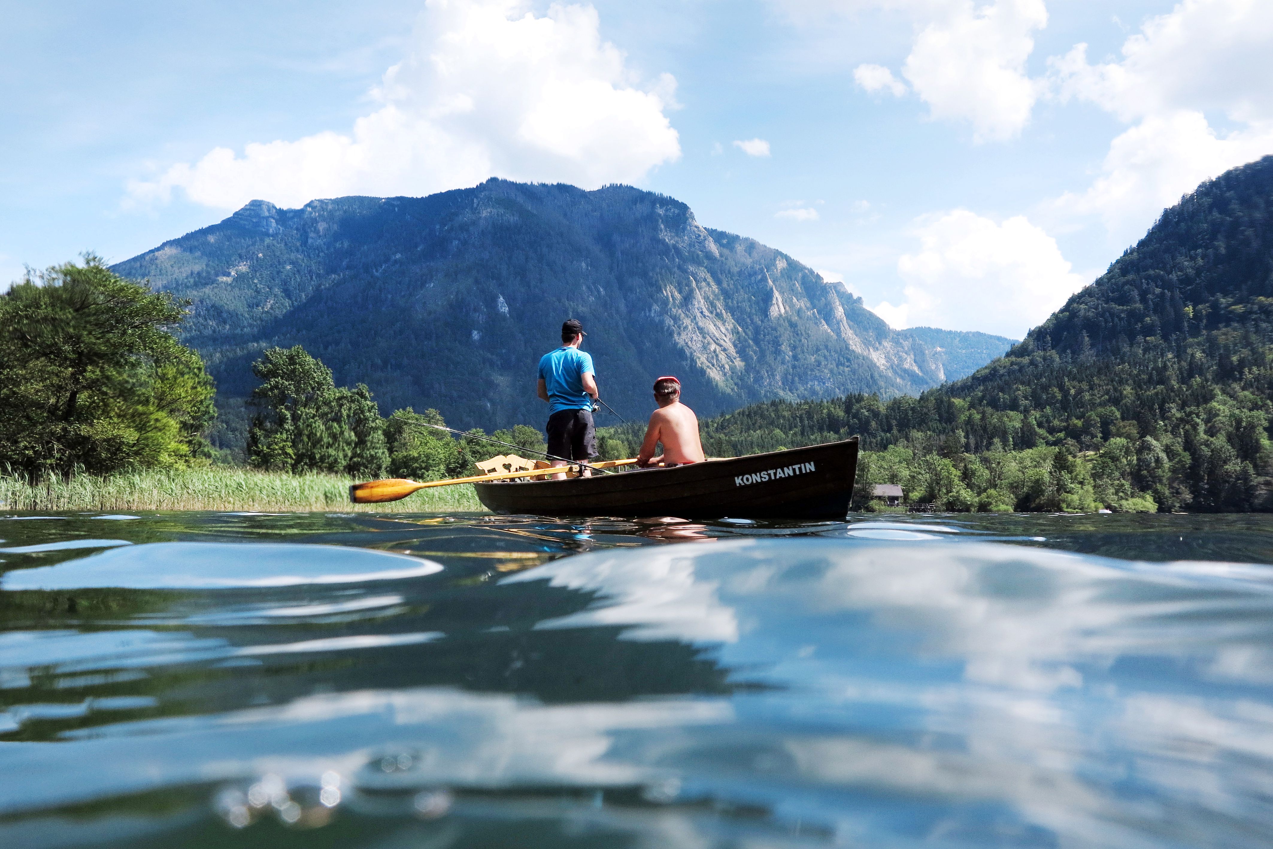 Zwei Personen in einem Boot auf einem See, umgeben von Bergen und Bäumen.
