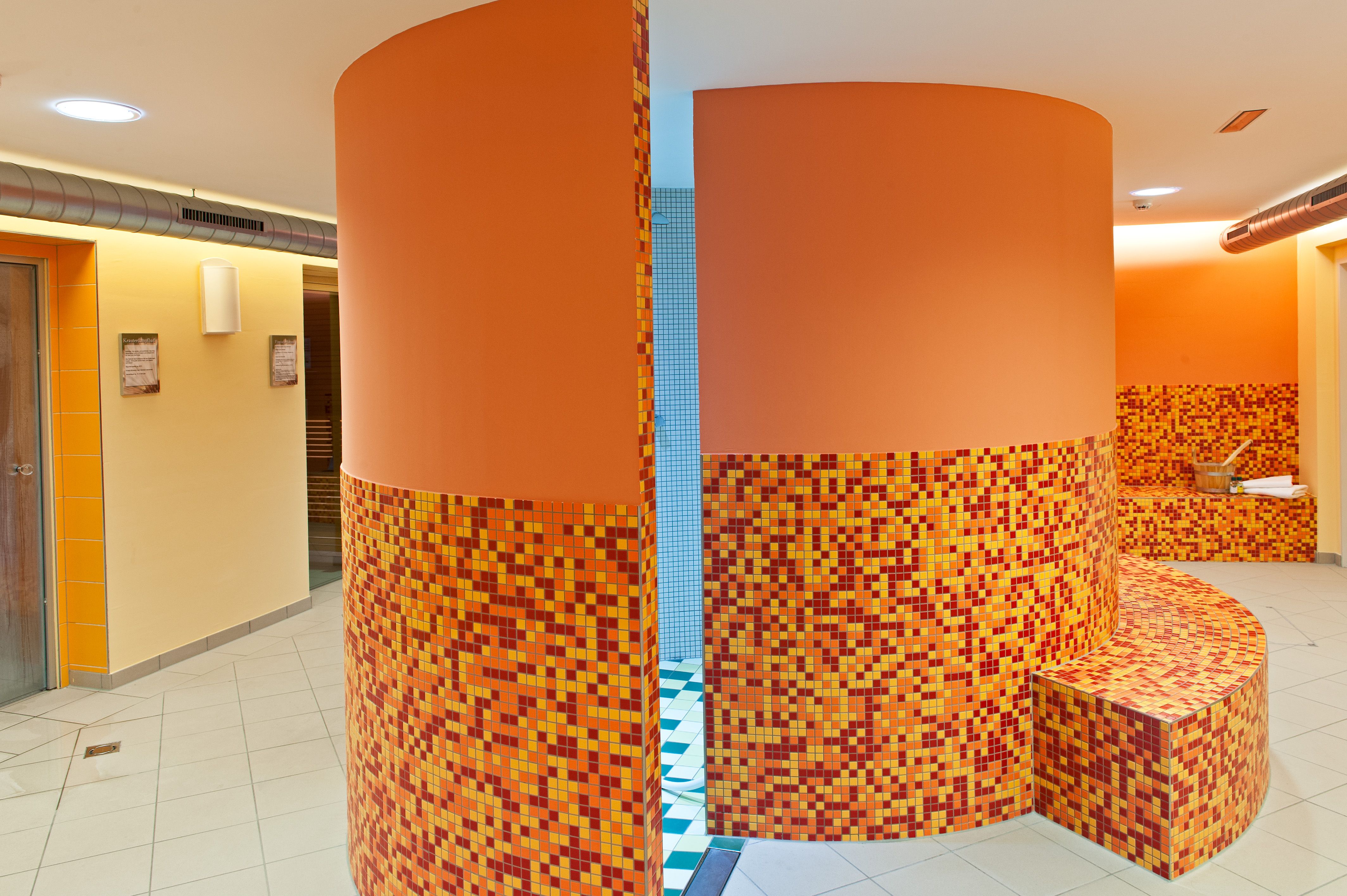 Innenansicht eines Wellnessbereichs mit orangefarbenen Mosaikfliesen und runden Wänden.