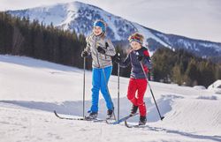 Zwei fröhliche Kinder gleiten über die schneebedeckten Loipen und genießen die frische Winterluft. Umgeben von majestätischen Bergen und glitzerndem Schnee, strahlt ihre Begeisterung für das Langlaufen in jeder Bewegung. Ein unvergessliches Winterabenteuer im Mostviertel wartet auf alle, die die Natur lieben.