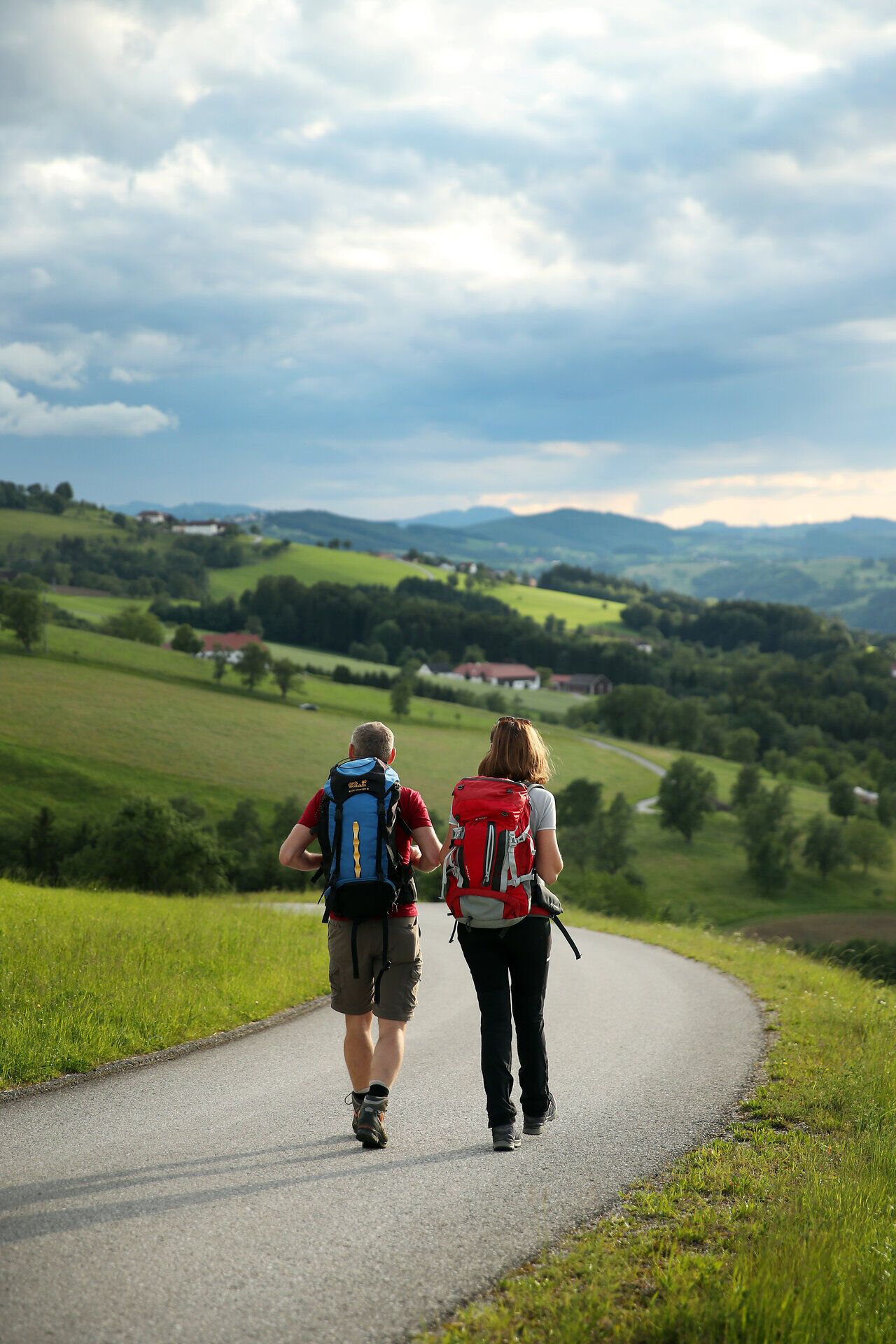 Pilgernde marschieren auf Straße durch Hügellandschaft.