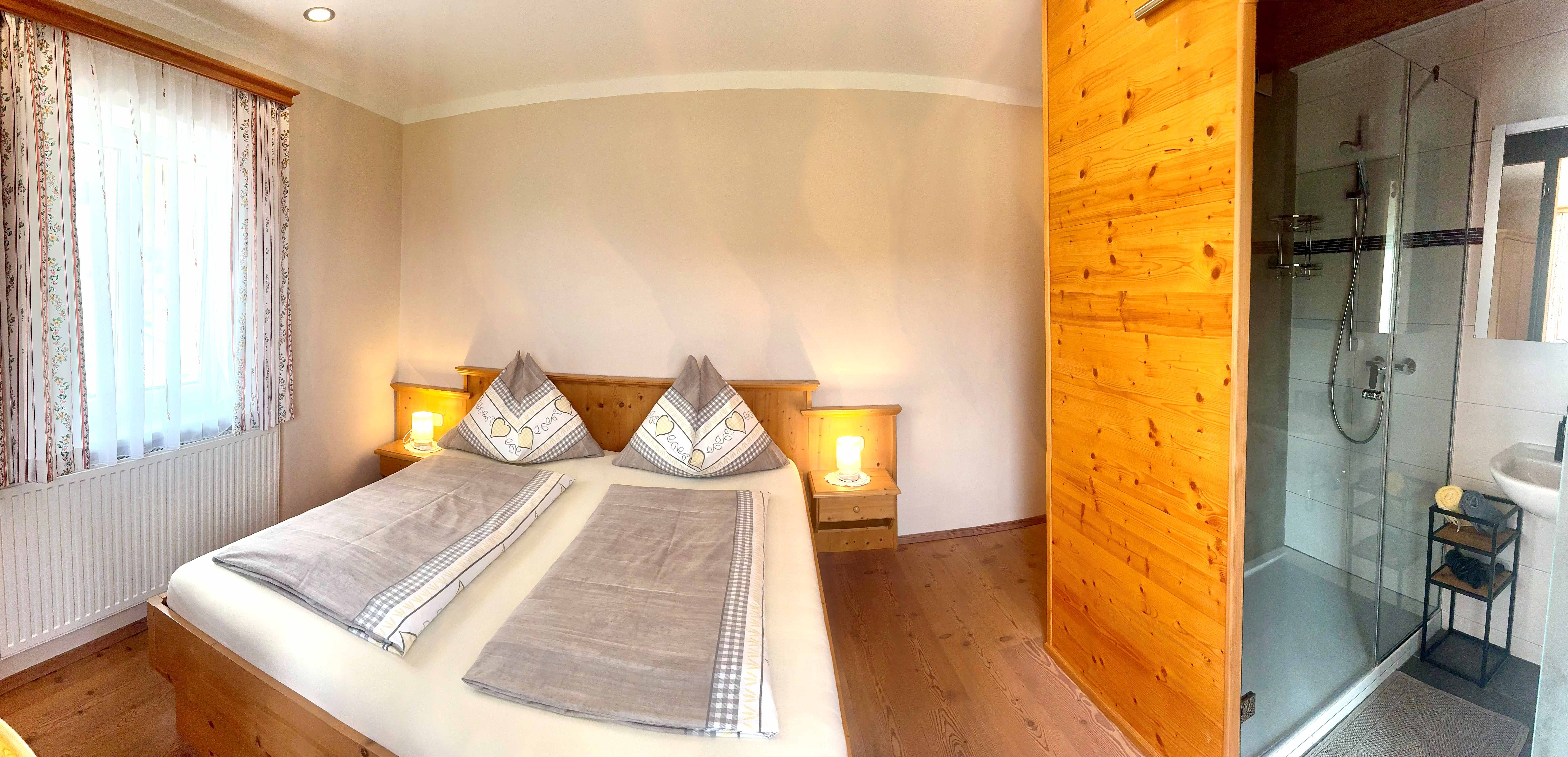Gemütliches Schlafzimmer mit Doppelbett, Holzmöbeln und angrenzendem Badezimmer mit Dusche.