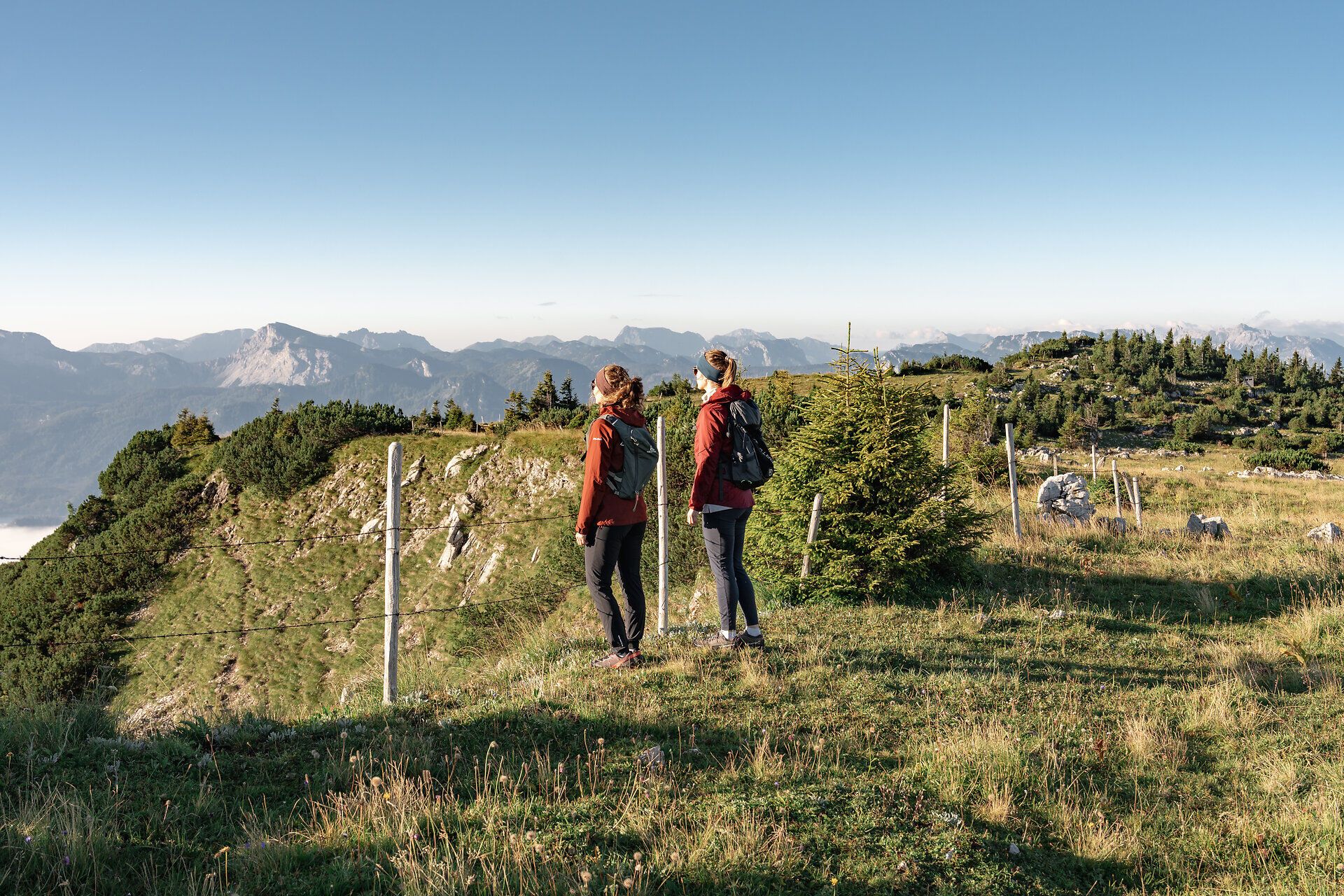 Die sanften Hügel der Ybbstaler Alpen erstrahlen im warmen Licht des Sonnenaufgangs. Zwei Wanderer genießen den atemberaubenden Ausblick auf die majestätischen Berge und die unberührte Natur, während die frische Morgenluft ihre Sinne belebt. Ein perfekter Moment, um die Ruhe und Schönheit der alpinen Landschaft zu erleben.