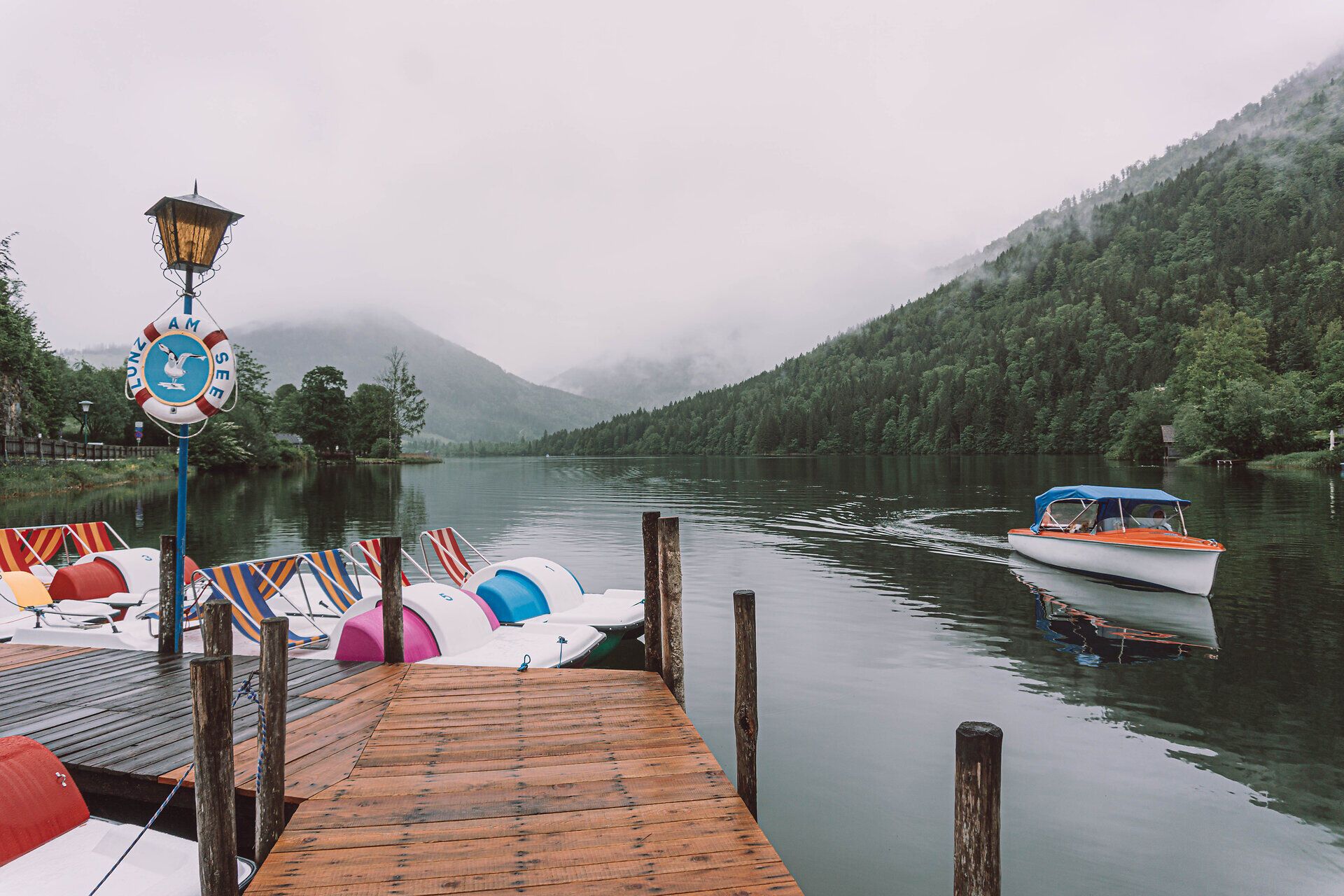 Der ruhige See, umgeben von sanften Hügeln und dichten Wäldern, lädt zu einem entspannten Tag in der Natur ein. Die sanften Wellen spiegeln die grauen Wolken wider, während ein Boot gemächlich über die Wasseroberfläche gleitet. Hier, wo die Stille der Berge auf die frische Luft trifft, findet jeder Besucher einen Ort der Erholung.