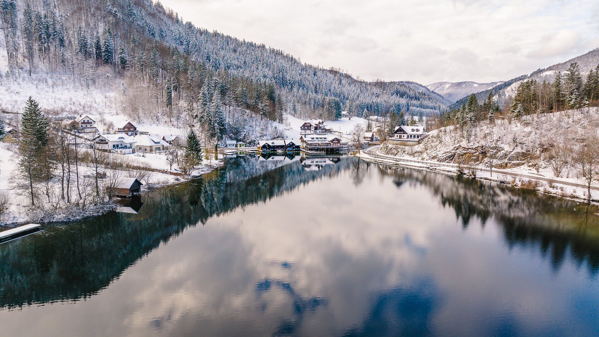 Die winterliche Landschaft um den See verzaubert mit einer schimmernden Schneedecke, die die umliegenden Berge sanft umhüllt. Die ruhige Wasseroberfläche spiegelt die majestätische Kulisse wider und lädt zu einem besinnlichen Spaziergang ein.