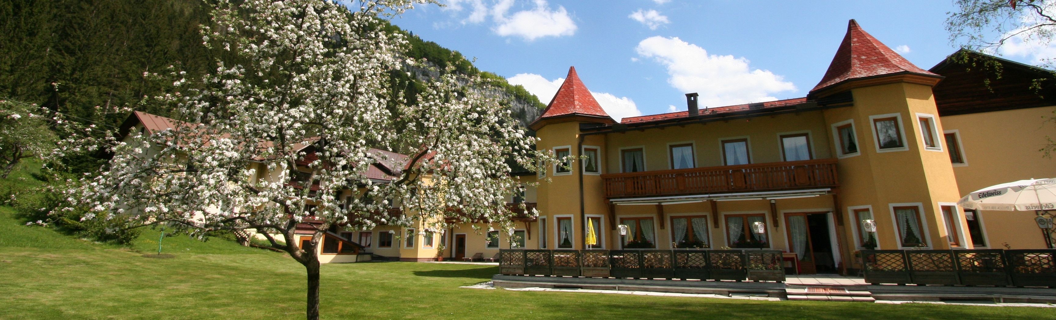 Ein gelbes Hotel mit roten Dächern und einem blühenden Baum im Vordergrund.