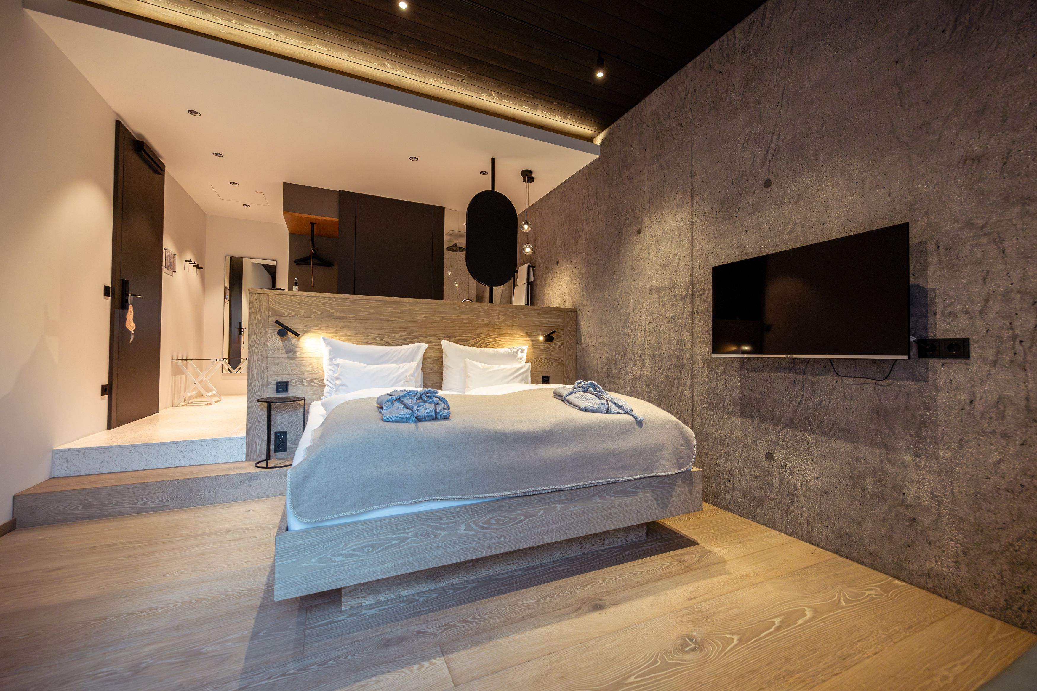 Modernes Schlafzimmer mit Holzfußboden, grauer Wand, Doppelbett und Flachbildfernseher.