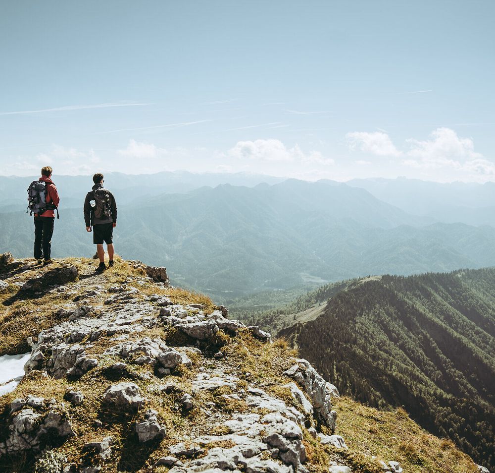 Zwei Wanderer stehen am Gipfel und genießen den atemberaubenden Blick über die Ybbstaler Alpen. Die frische Bergluft und die majestätischen Landschaften laden dazu ein, die Seele baumeln zu lassen und die Schönheit der Natur zu erleben.