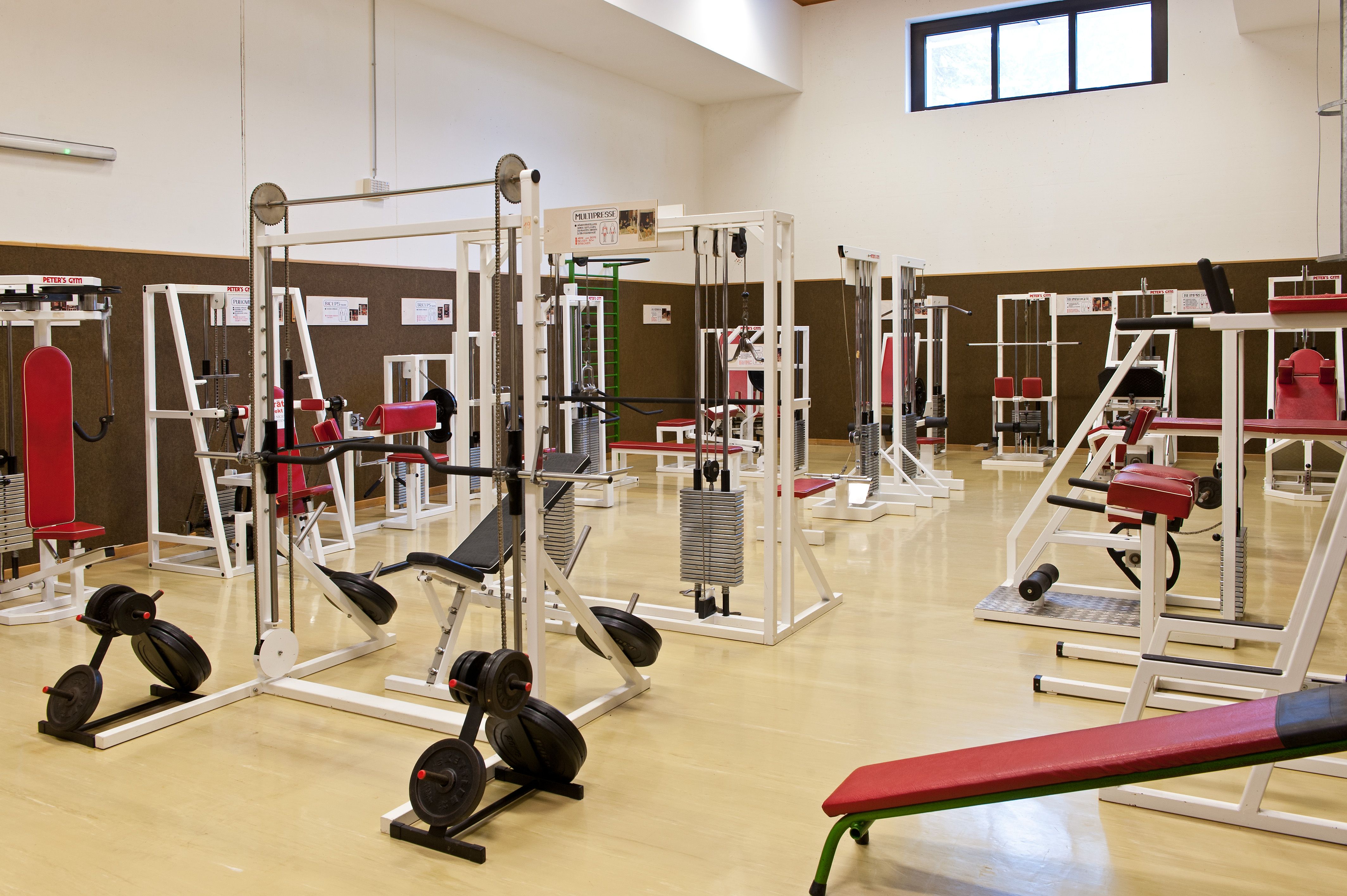 Fitnessstudio mit verschiedenen Trainingsgeräten und roten Polstern.