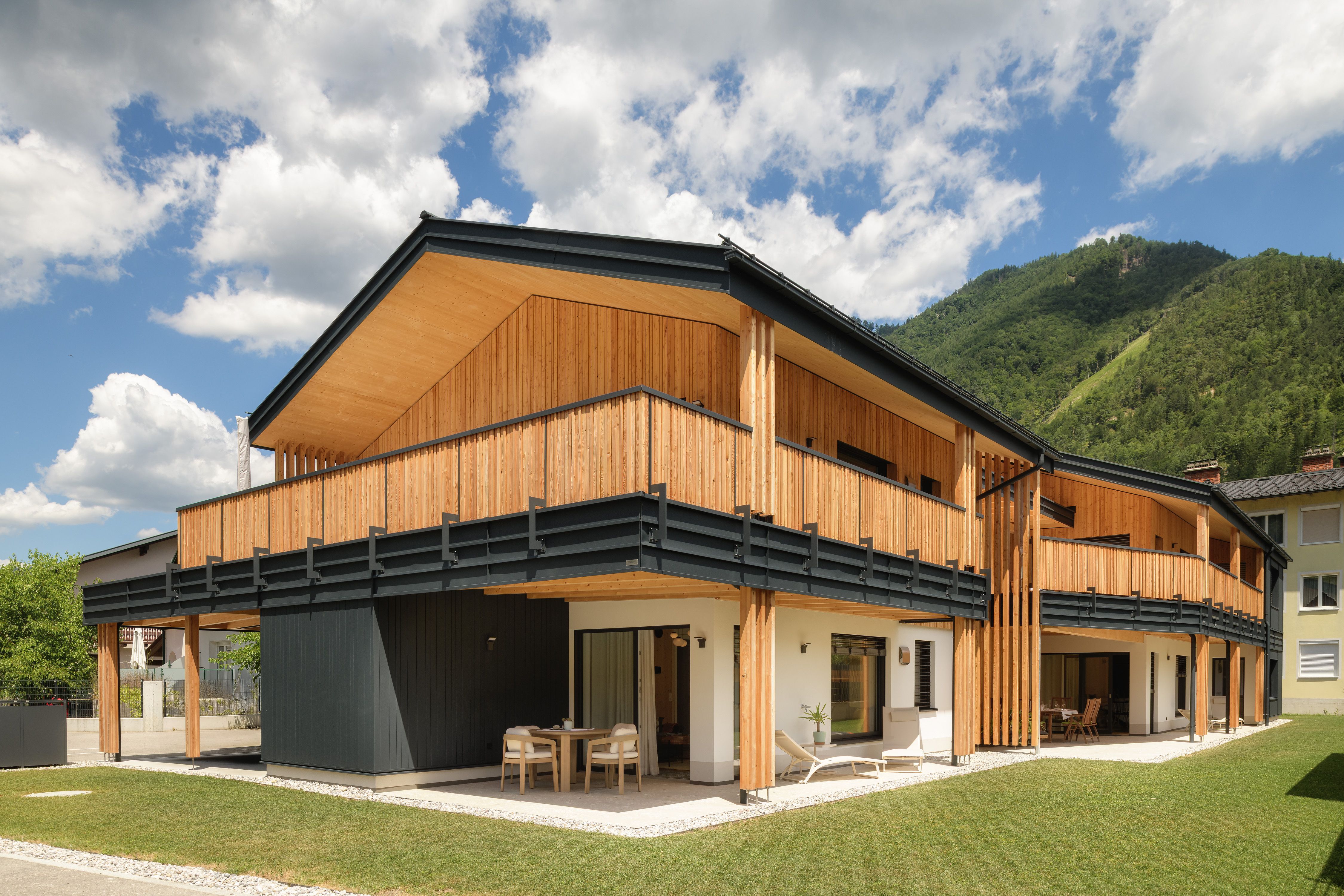Modernes Holzgebäude mit Balkon und Bergkulisse im Hintergrund.
