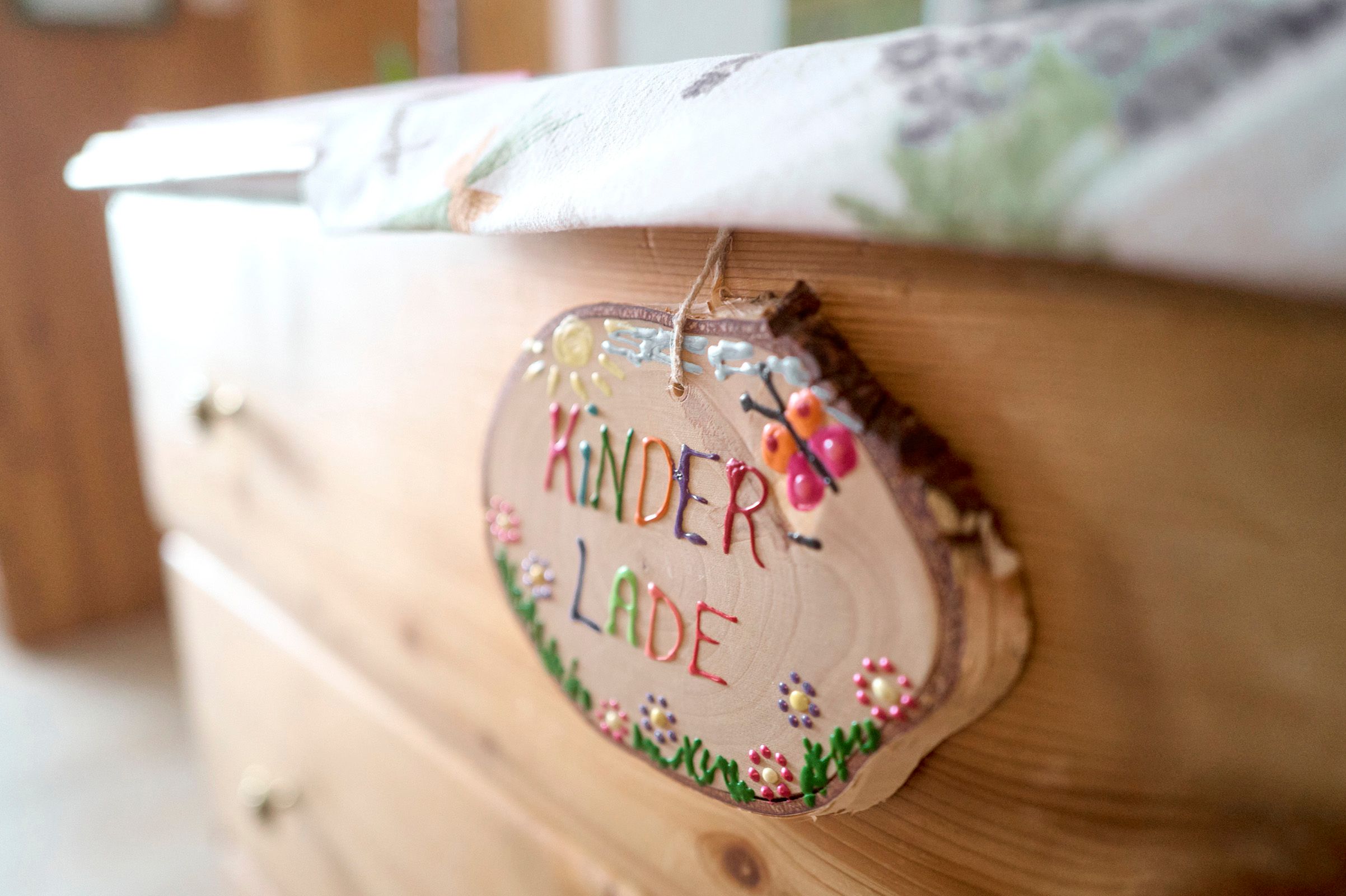 Nahaufnahme eines Holzschildes mit der Aufschrift 'Kinderlade' an einer Kommode.