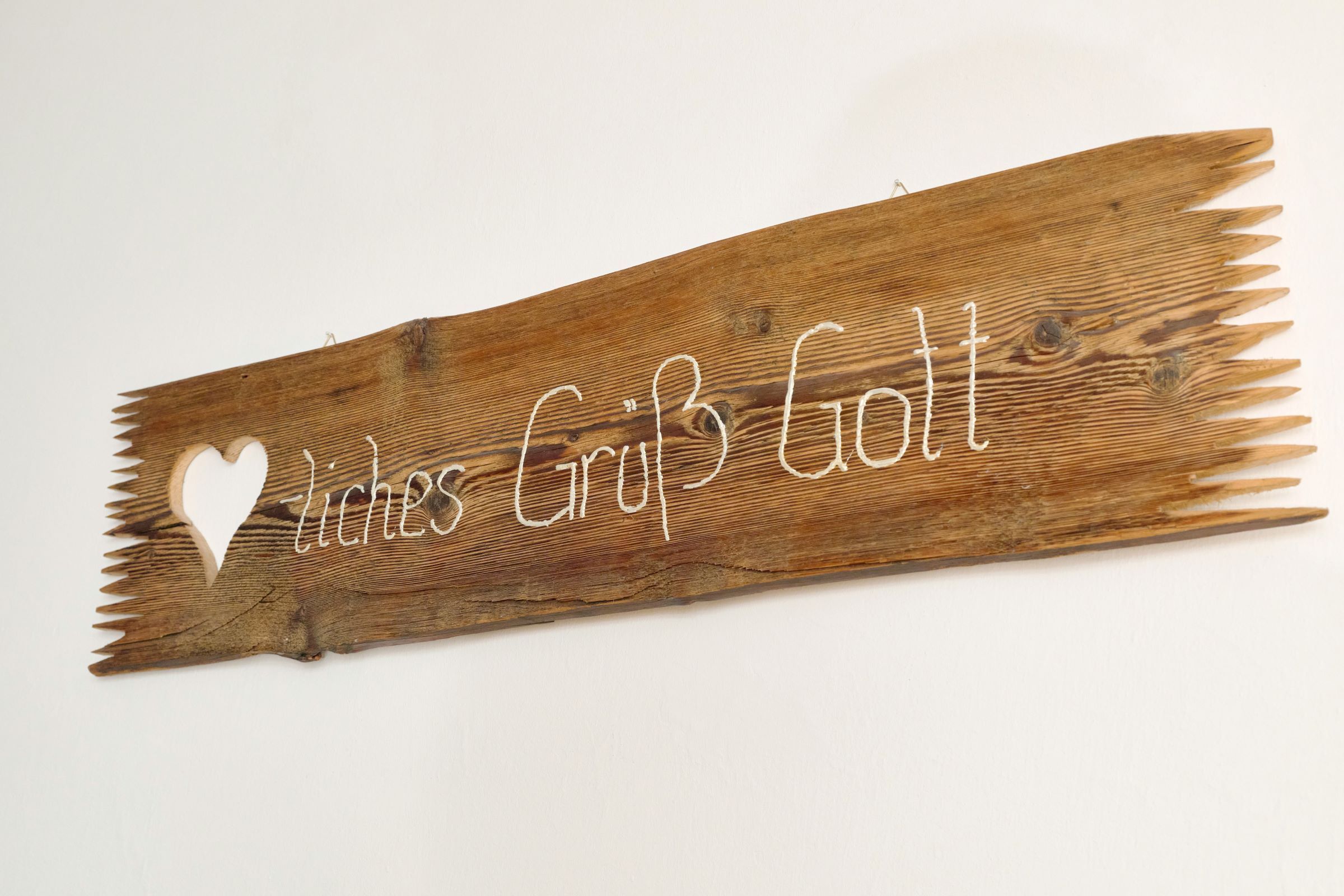 Holzschild mit der Aufschrift 'Herzliches Grüß Gott' und einem Herzsymbol.