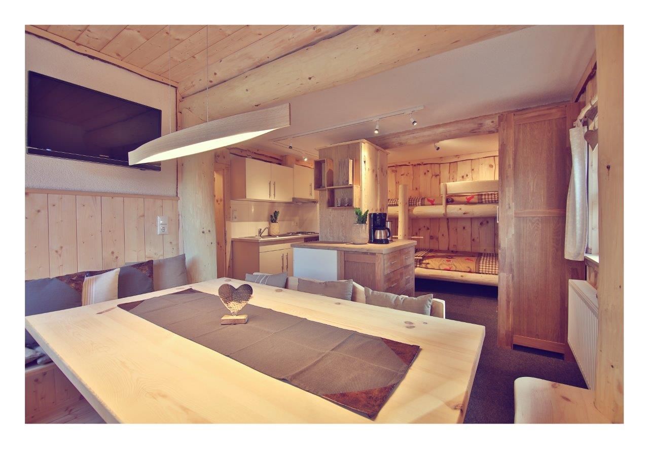 Innenansicht eines gemütlichen Chalets mit Holzmöbeln, Esstisch, Küche und Etagenbetten.