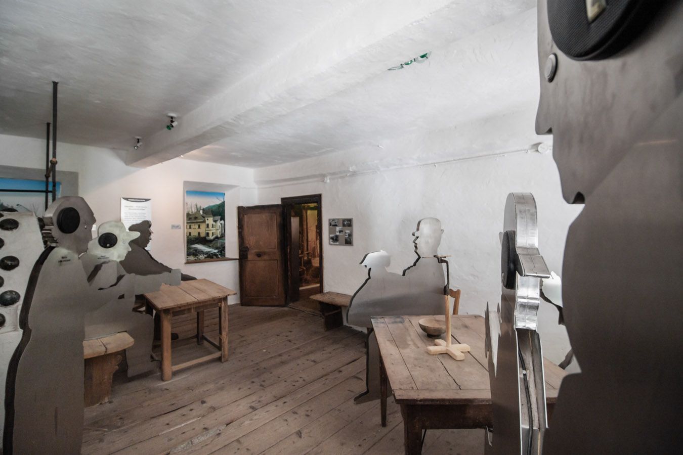 Innenraum mit Holzfußboden und Metallfiguren an Holztischen.