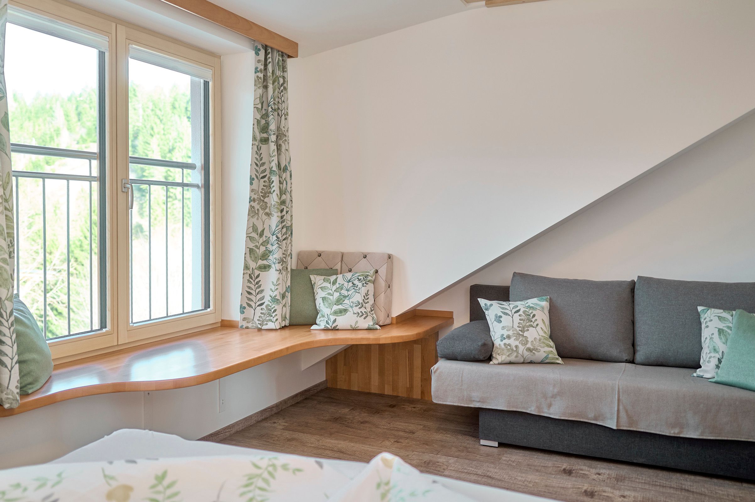 Wohnzimmer mit großem Fenster, grauem Sofa und Holzboden.