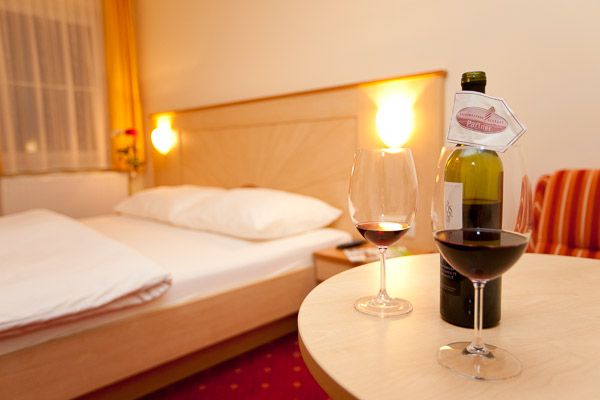 Ein gemütliches Hotelzimmer mit einem Doppelbett, zwei Weingläsern und einer Weinflasche auf einem Tisch.