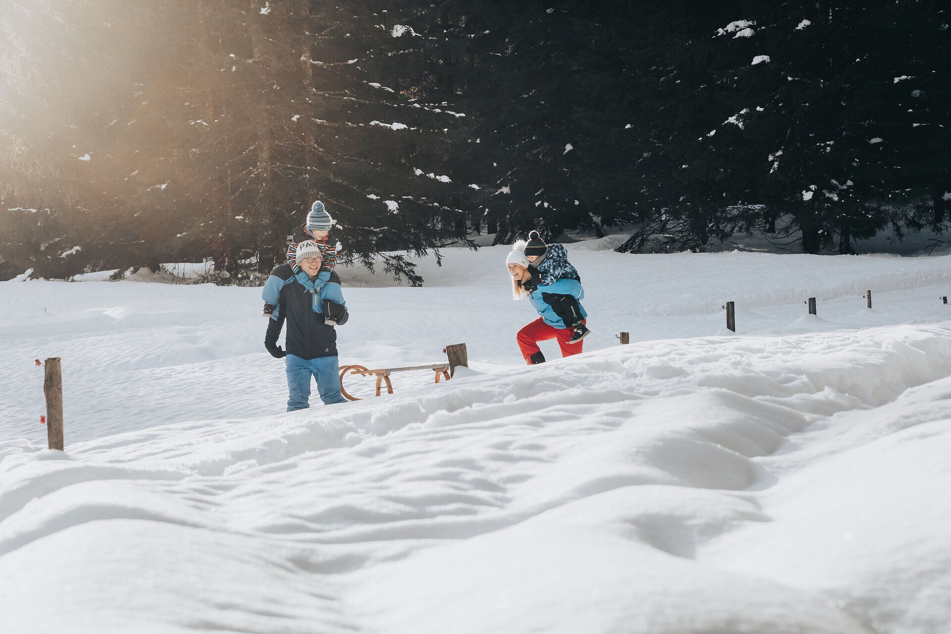 Eine Familie genießt den Winter in der verschneiten Landschaft der Ybbstaler Alpen. Die Kinder lachen und spielen im frischen Schnee, während die Sonne sanft durch die Bäume scheint und eine magische Atmosphäre schafft.
