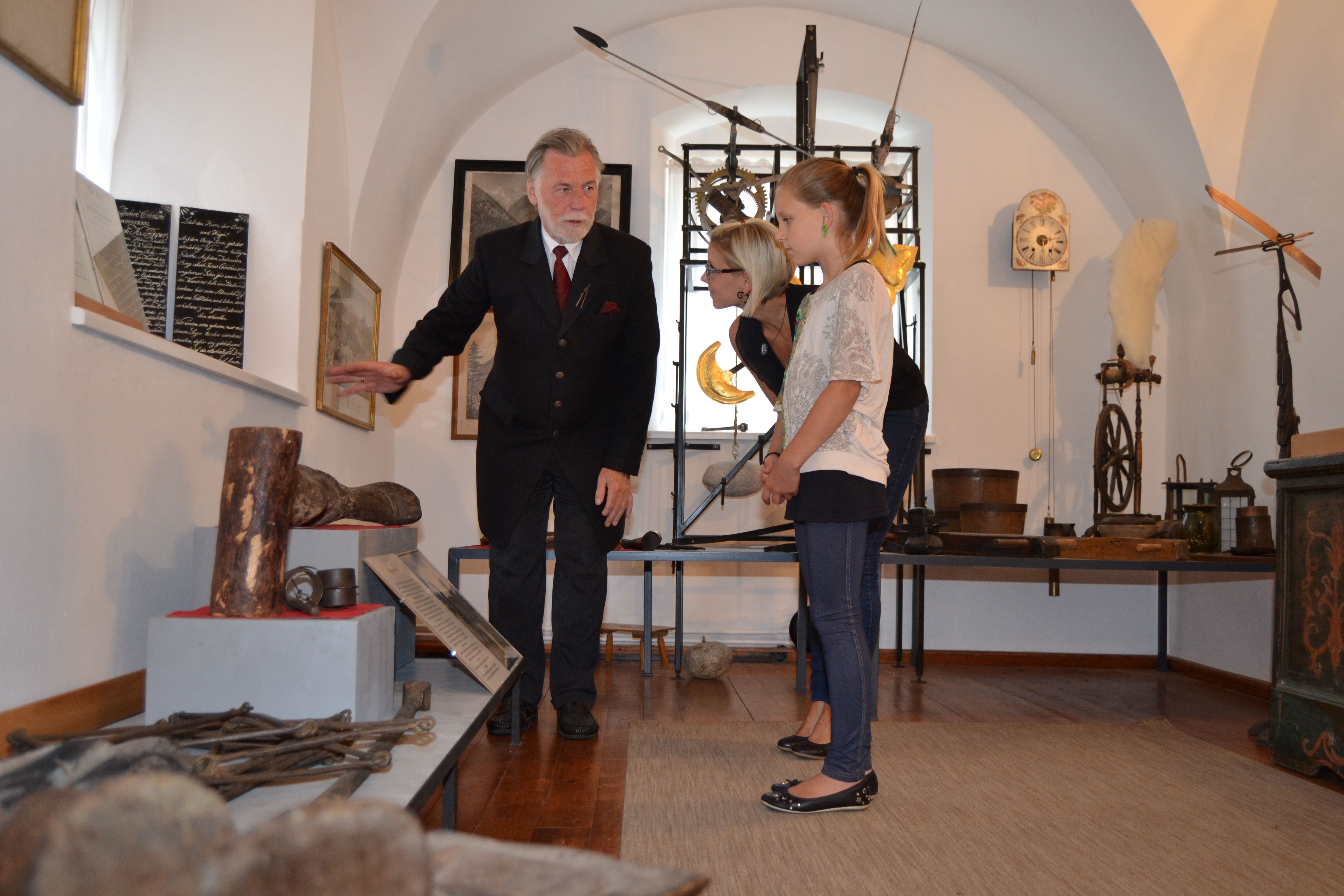 Ein älterer Mann zeigt zwei Frauen historische Objekte in einem Museum.