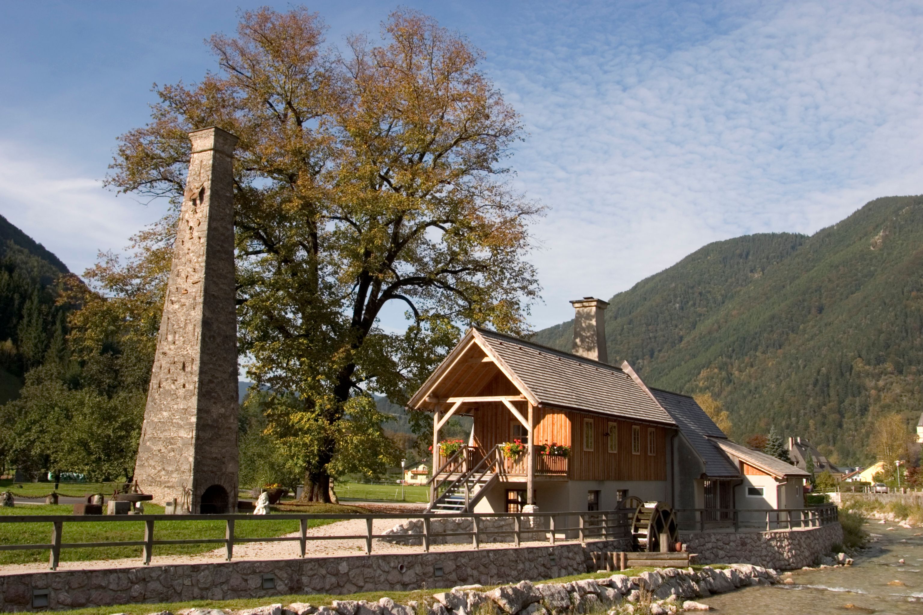 Historisches Gebäude mit Schornstein und Wasserrad in ländlicher Umgebung.