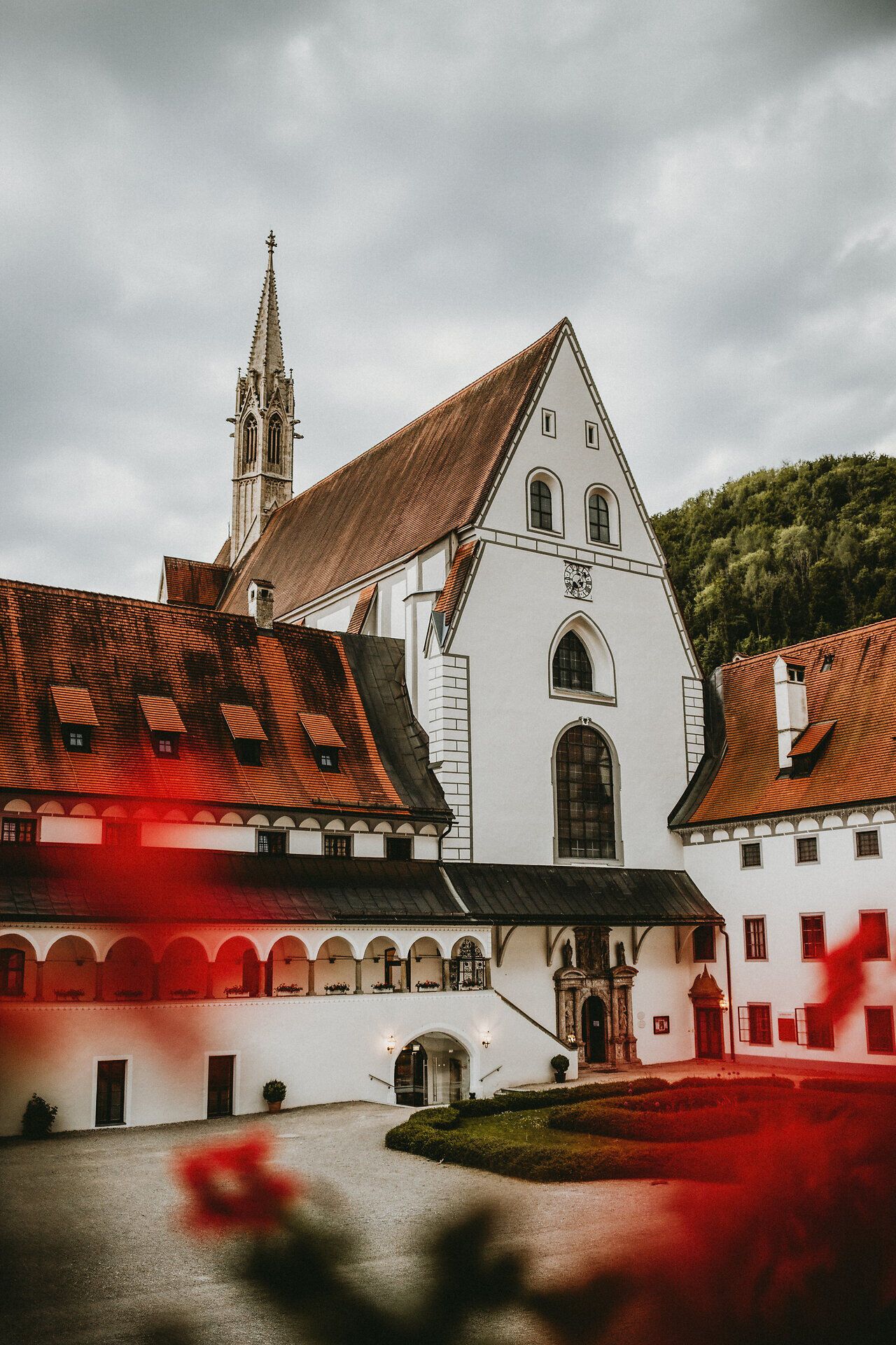 Die majestätische Kartause Gaming erhebt sich stolz zwischen sanften Hügeln, umgeben von üppigem Grün und blühenden Pflanzen. Die beeindruckende Architektur des Klosters strahlt Ruhe und Gelassenheit aus, während die Wolken am Himmel eine dramatische Kulisse schaffen. Ein Ort, der zum Verweilen und Entdecken einlädt.