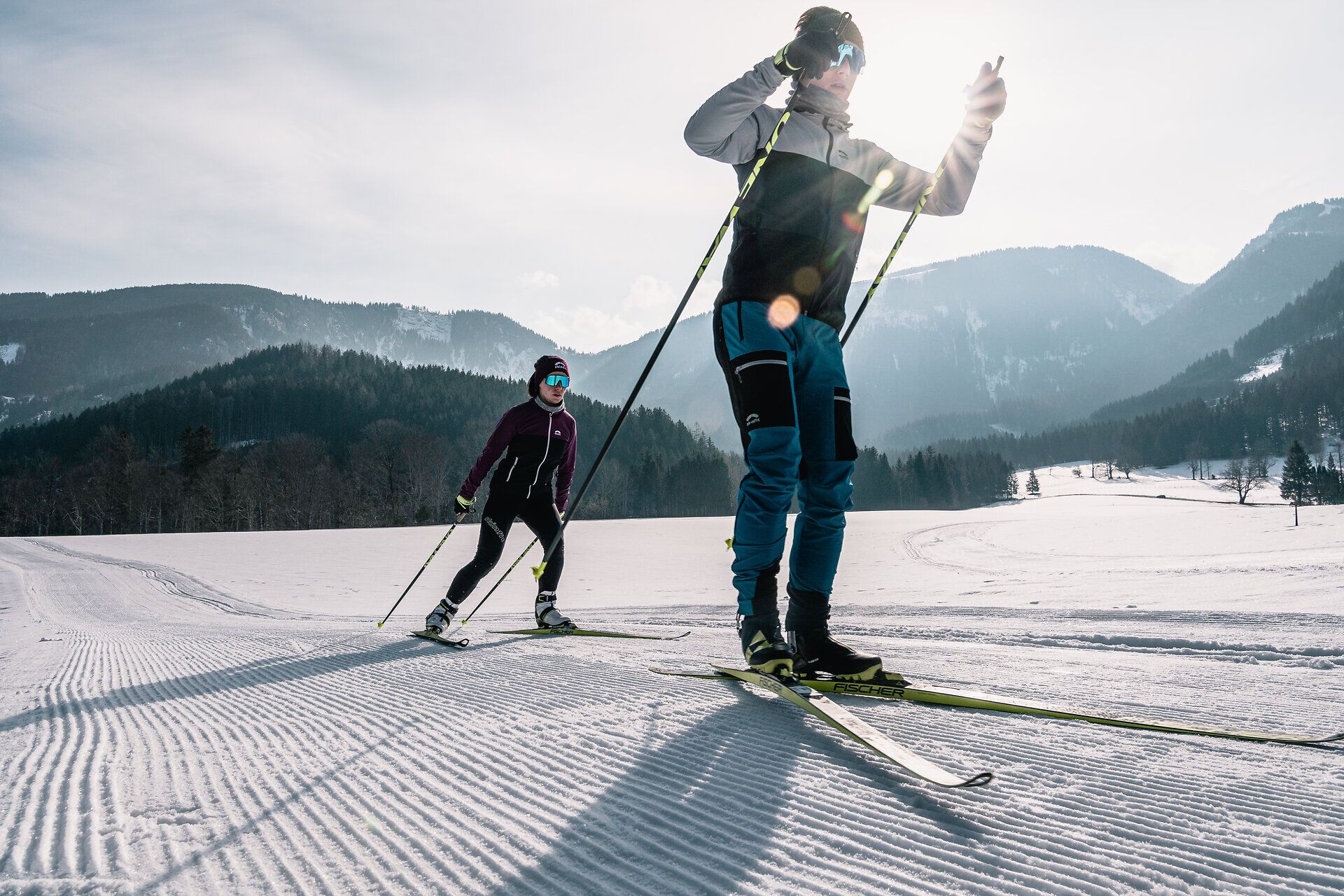 Die glitzernde Schneedecke erstreckt sich über die sanften Hügel der Ybbstaler Alpen, während zwei Skilangläufer in perfekter Harmonie mit der winterlichen Landschaft ihre Spuren ziehen. Die klare, kalte Luft und die strahlende Sonne schaffen eine einladende Atmosphäre für einen aktiven Winterurlaub.