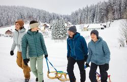Eine fröhliche Familie genießt den Wintertag in der verschneiten Landschaft. Mit Rodeln in der Hand und strahlenden Gesichtern machen sie sich auf den Weg, um die Abfahrt zu erleben. Die schneebedeckten Bäume und die klare Luft schaffen eine unvergessliche Atmosphäre.