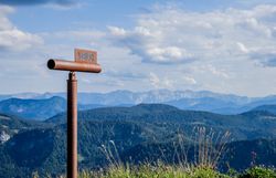 Die majestätischen Gipfel des Großen Ötschers erheben sich stolz gegen den klaren Himmel, während die sanften Hügel und blühenden Wiesen eine einladende Kulisse für Wanderer bieten. Ein Fernrohr lädt dazu ein, die atemberaubende Aussicht zu genießen und die Schönheit der Natur in vollen Zügen zu erleben.