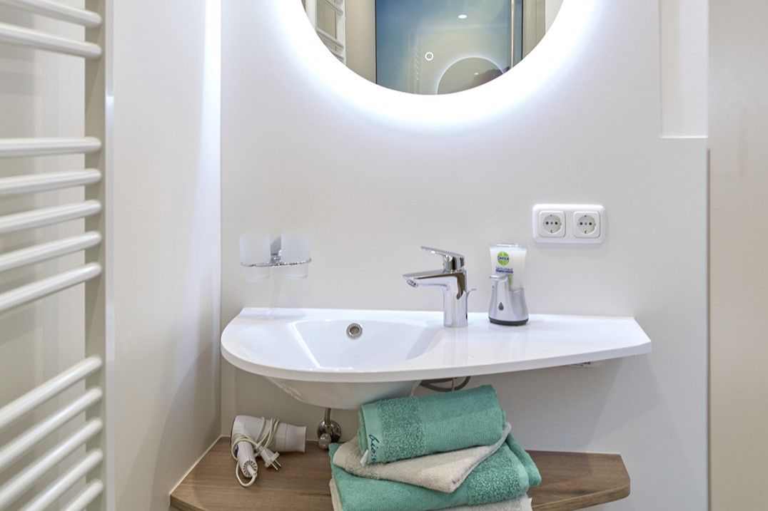 Modernes Badezimmer mit rundem Spiegel, Waschbecken und Handtüchern.