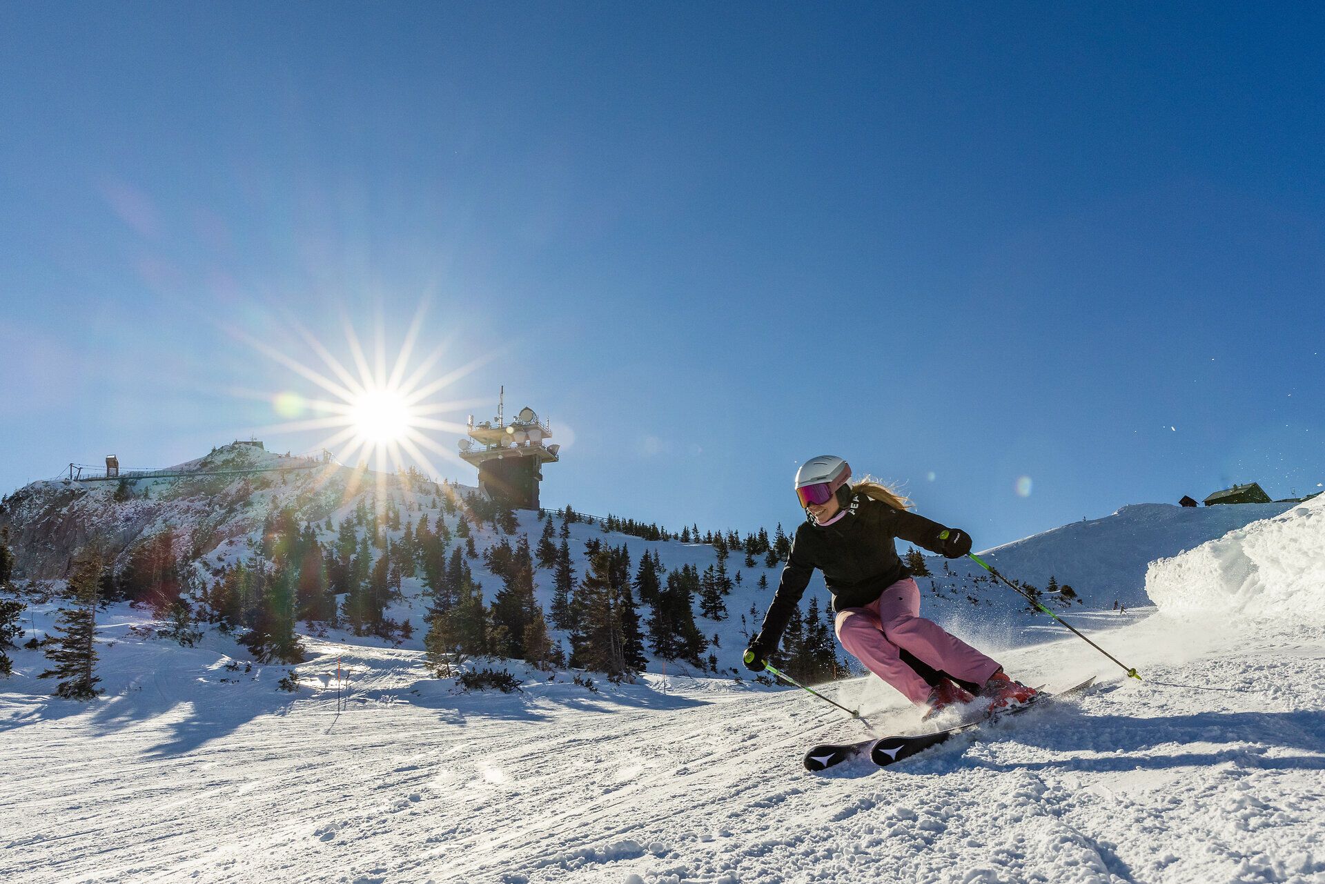 Die strahlende Wintersonne taucht die verschneite Landschaft in ein warmes Licht, während eine Skifahrerin elegant die Pisten hinuntergleitet. Umgeben von den majestätischen Ybbstaler Alpen bietet dieser Ort ein unvergessliches Erlebnis für Wintersportliebhaber. Hier wird der Winter zum Abenteuer und die Natur zur perfekten Kulisse.