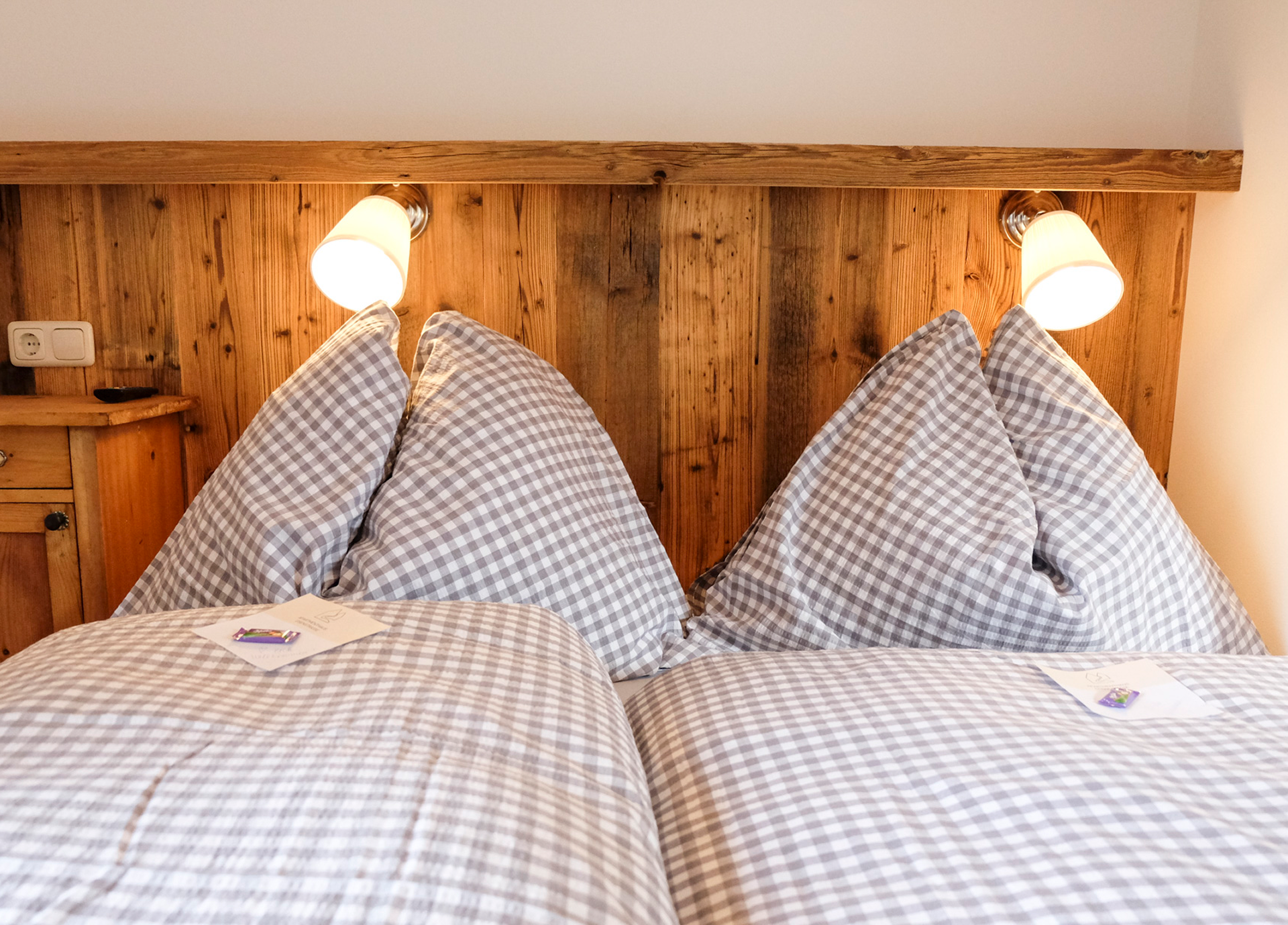 Ein gemütliches Doppelbett mit karierten Bettbezügen und zwei Leselampen an einem Holzkopfteil.