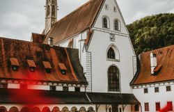 Die majestätische Kartause Gaming erhebt sich stolz zwischen sanften Hügeln, umgeben von üppigem Grün und blühenden Pflanzen. Die beeindruckende Architektur des Klosters strahlt Ruhe und Gelassenheit aus, während die Wolken am Himmel eine dramatische Kulisse schaffen. Ein Ort, der zum Verweilen und Entdecken einlädt.