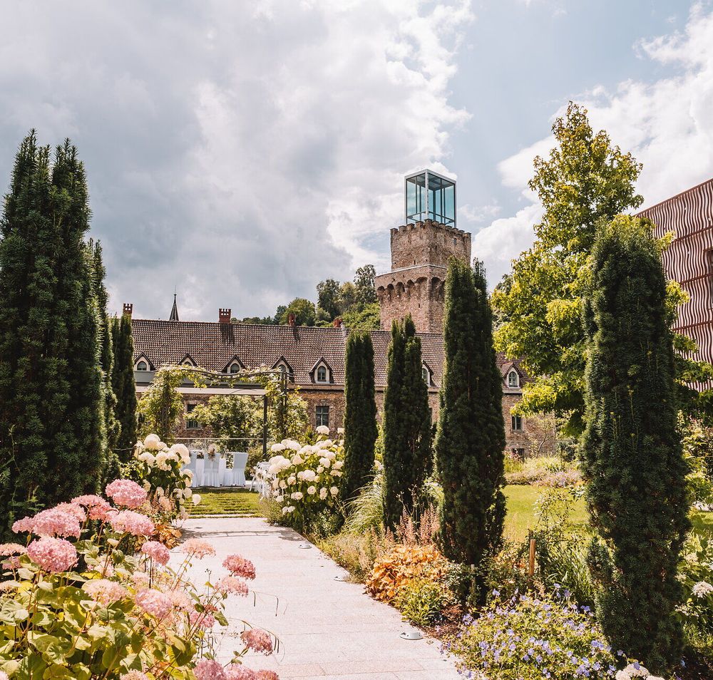 Blühender Schlossgarten von Schloss Rothschild in Waidhofen an der Ybbs mit Blumenbeeten, schlanken Zypressen und dem gläsernen Turm des historischen Gebäudes