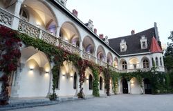 Umgeben von üppigem Grün und historischen Mauern strahlt das Schloss Rothschild eine einladende Atmosphäre aus. Die sanften Bögen und die blühenden Pflanzen verleihen dem Ort einen Hauch von Romantik und laden dazu ein, die Schönheit der Natur zu genießen.