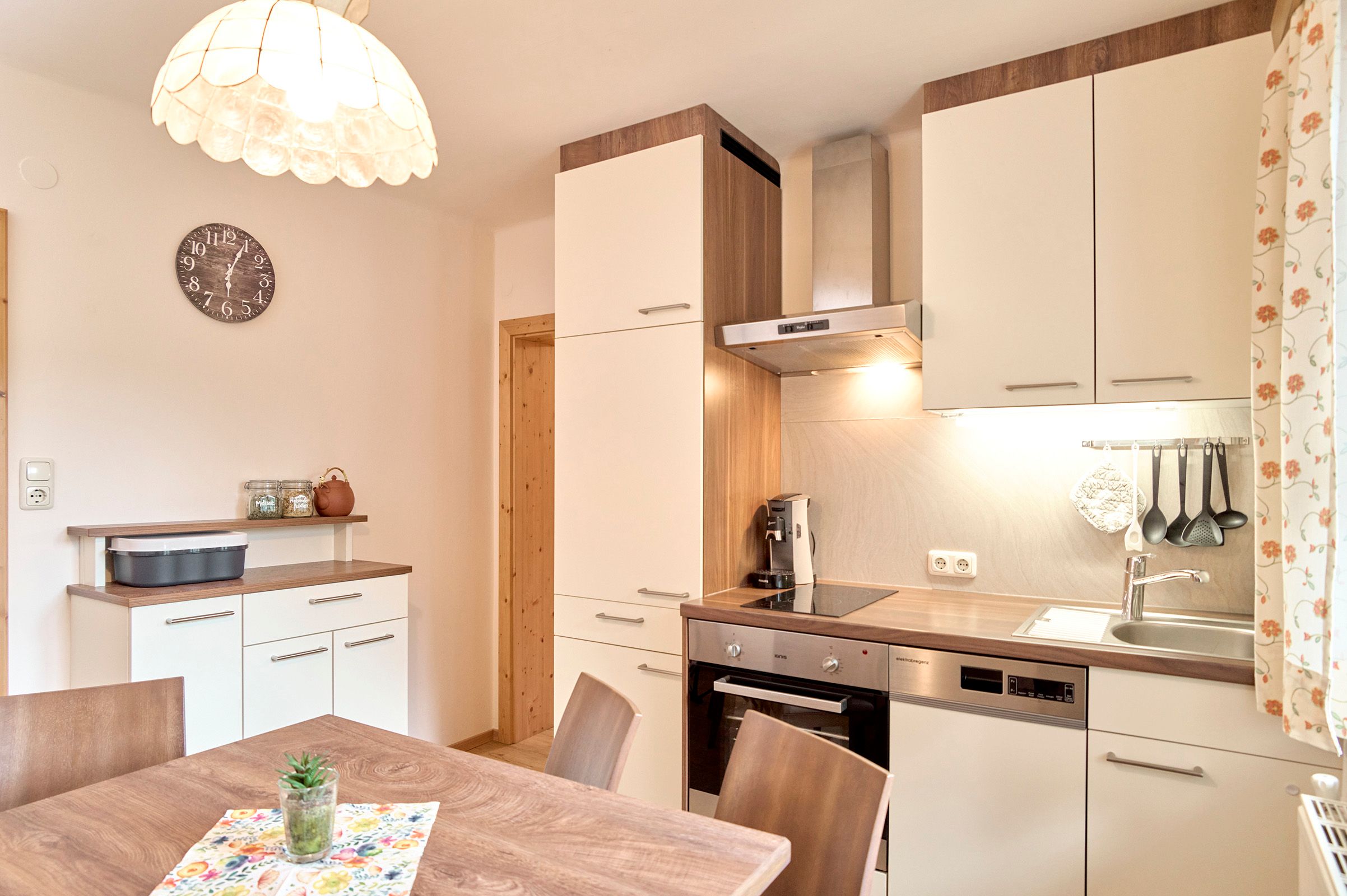 Moderne Küche mit Holz- und Weißtönen, Esstisch, Hängelampe und Küchengeräten.