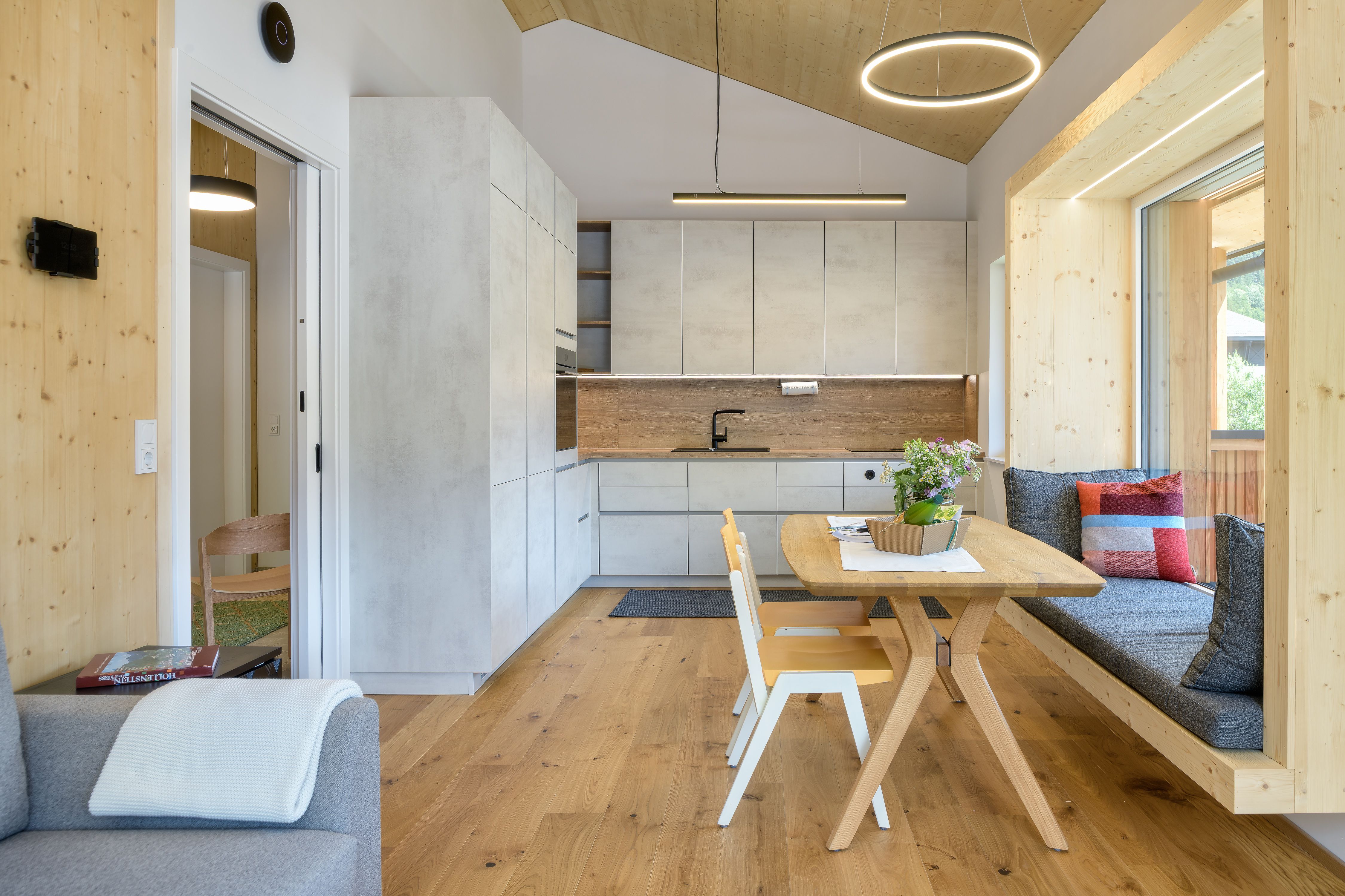 Moderne Küche mit Holz- und Betonoptik, Esstisch und Sitzbank am Fenster.