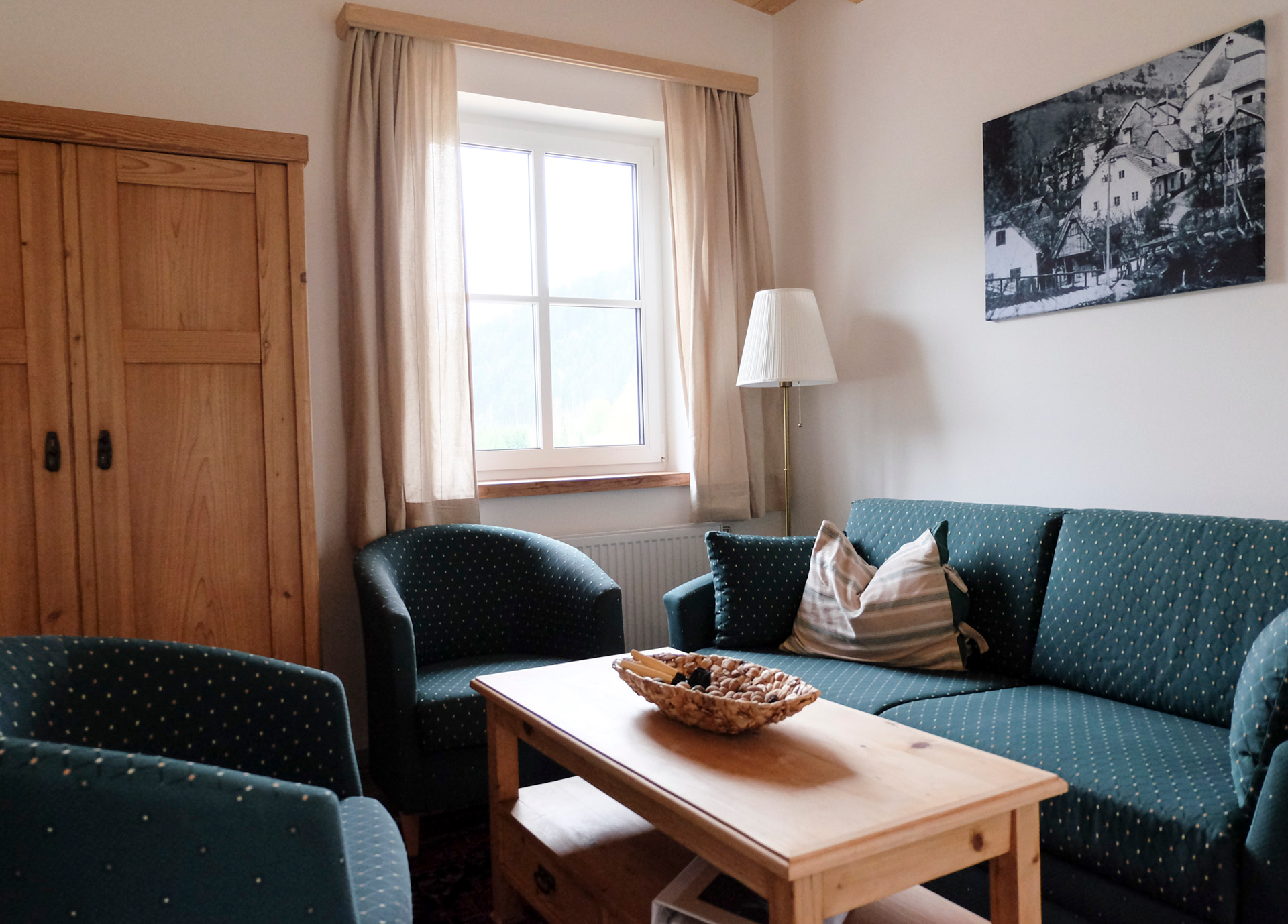 Gemütliches Wohnzimmer mit grünen Polstermöbeln, Holztisch und Fenster mit Vorhängen.