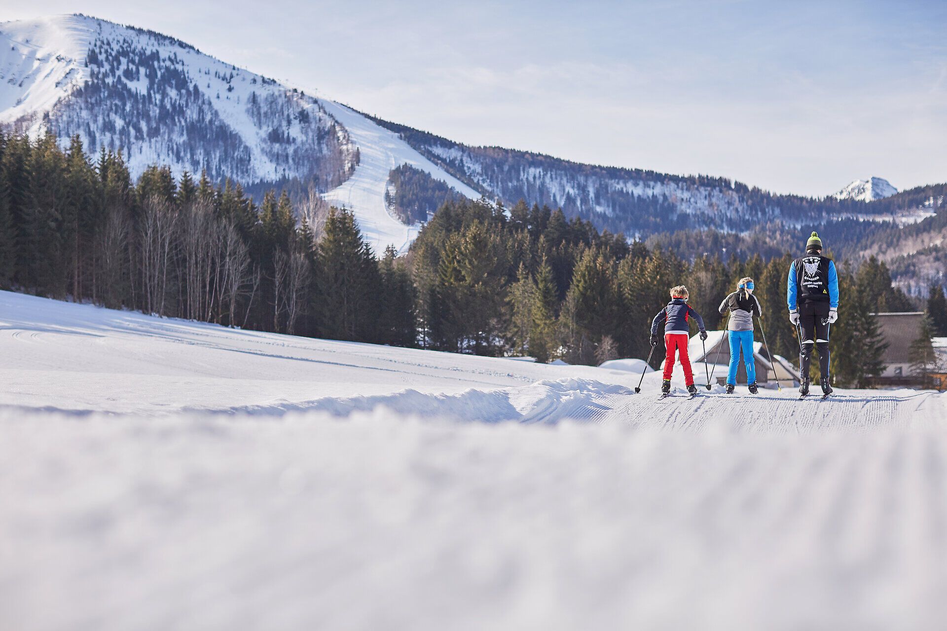 Die glitzernde Schneedecke erstreckt sich über die sanften Hügel, während die frische Winterluft die Sinne belebt. Langläufer gleiten harmonisch durch die verschneite Landschaft, umgeben von majestätischen Bäumen und der ruhigen Stille der Natur. Ein unvergessliches Erlebnis für alle, die die winterliche Idylle genießen möchten.