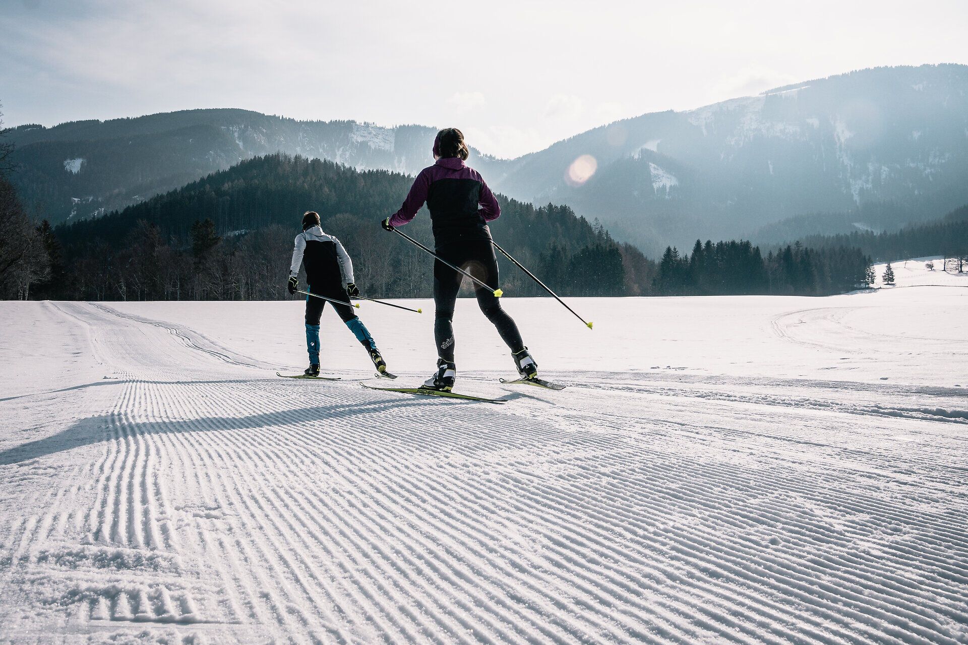 Die glitzernde Schneedecke erstreckt sich bis zum Horizont, während zwei Langläufer in harmonischem Rhythmus durch die winterliche Landschaft gleiten. Umgeben von den majestätischen Ybbstaler Alpen, bietet dieser Ort die perfekte Kulisse für einen aktiven Winterurlaub voller frischer Luft und unvergesslicher Erlebnisse.